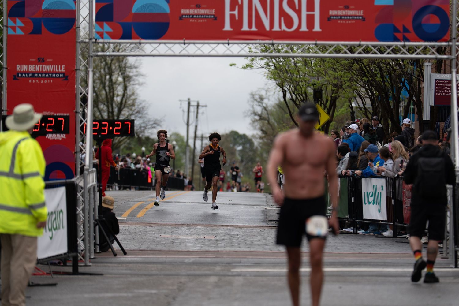 Runners crossing the finish line at the Run Bentonville Half Marathon race event on a cloudy day.