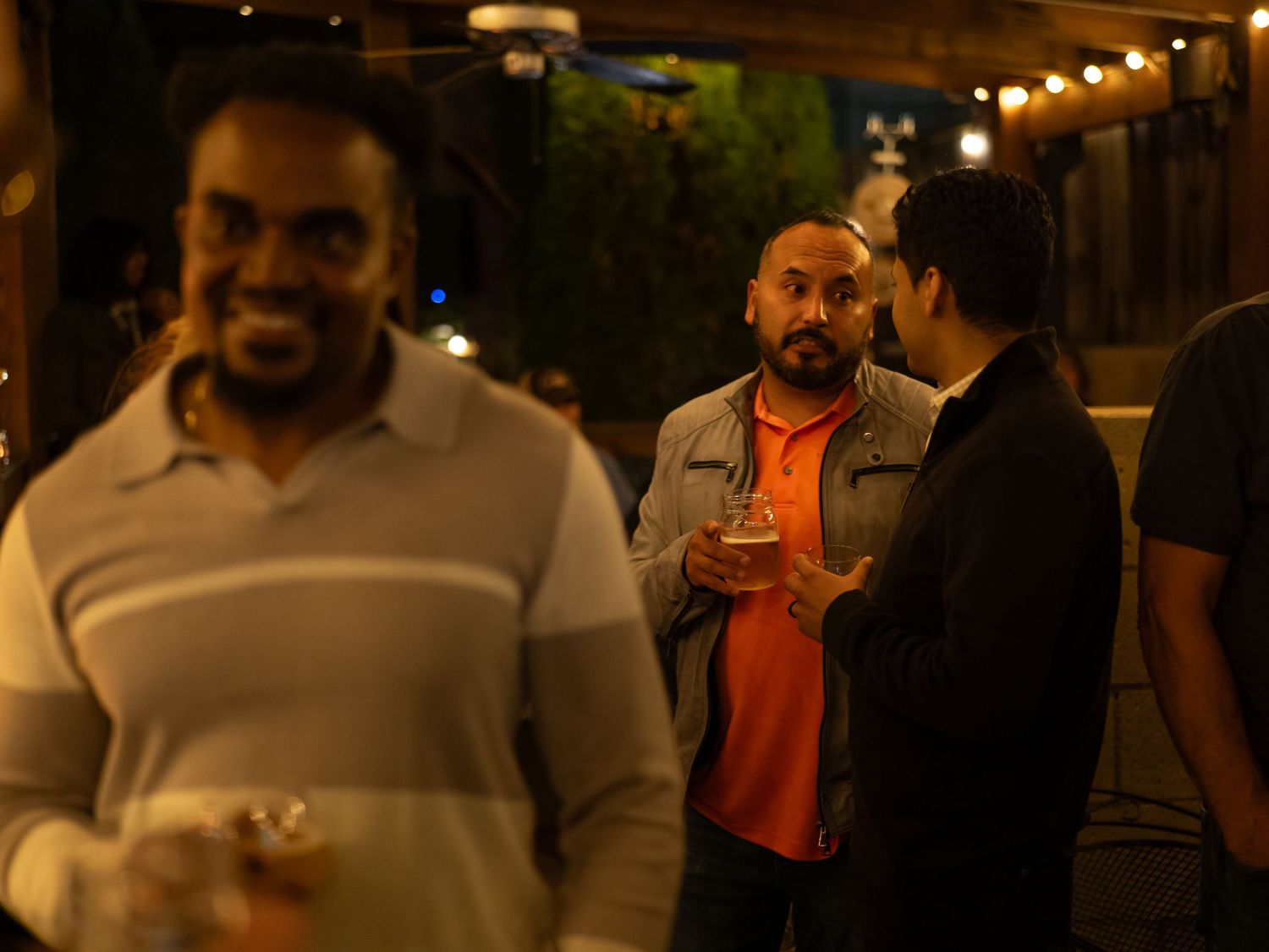 A group of people having a conversation at night under warm lighting at an outdoor venue.