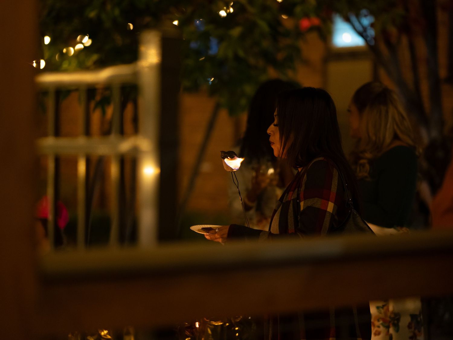 A person sits alone at night reading by candlelight through a window frame, creating a cozy ambiance.