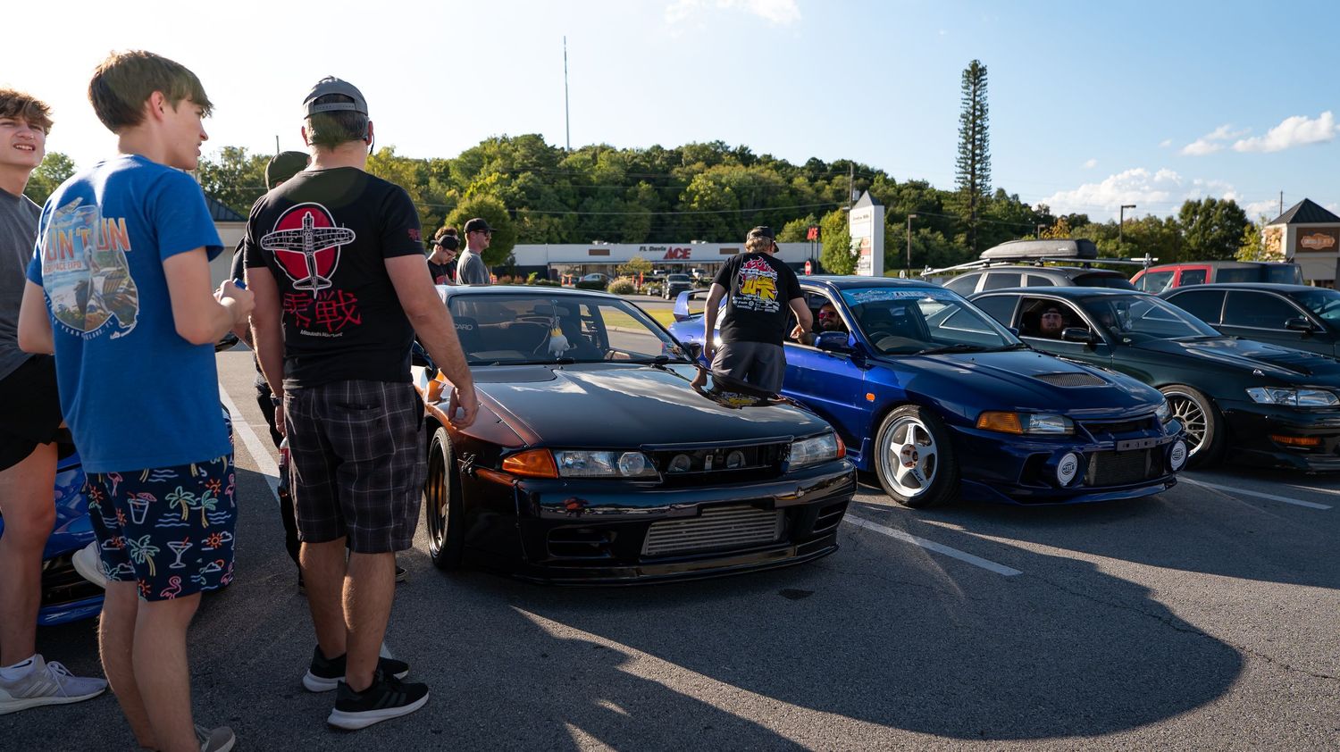 Group of car enthusiasts gathered around modified vehicles at outdoor meet.