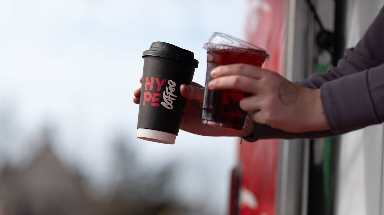 Coffee cups being exchanged between hands against a bright background.