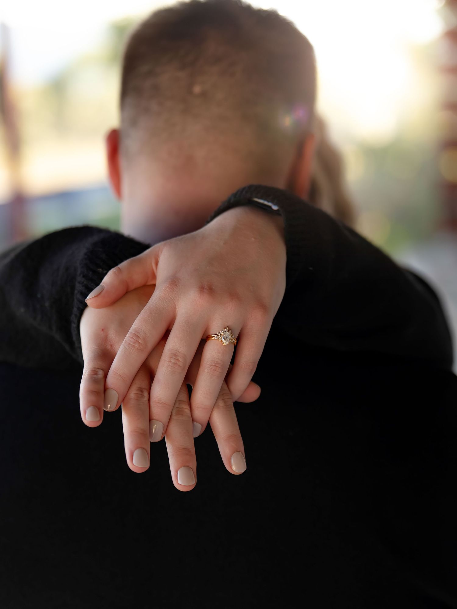 A detailed view of hands displaying an engagement ring against a dark background.