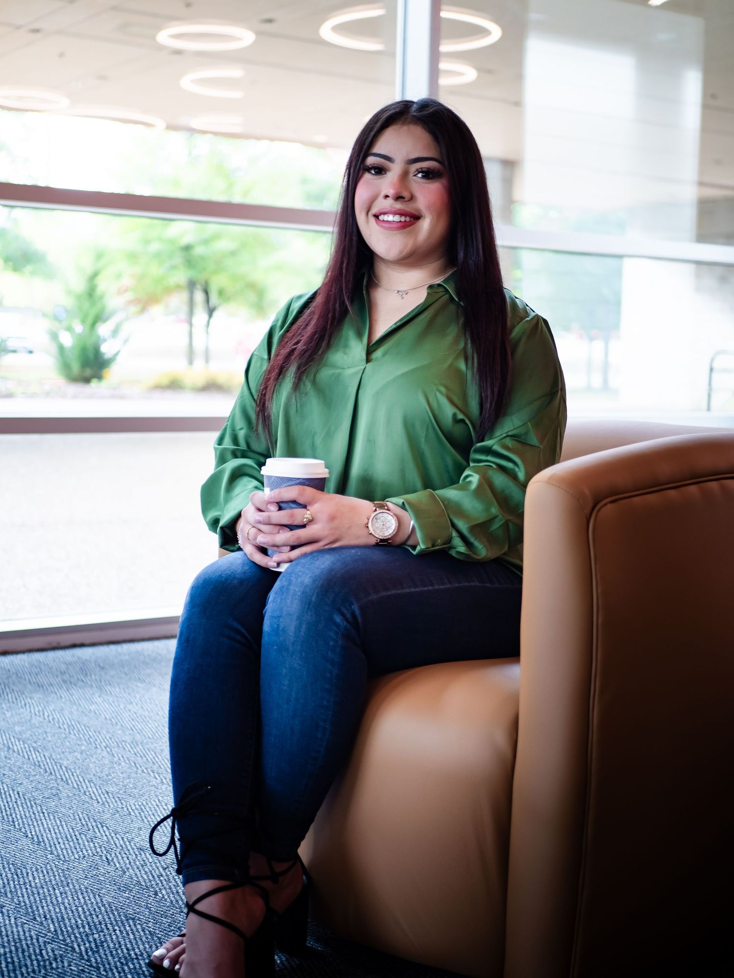 A person in a green top sits comfortably in a brown armchair in a modern interior space.