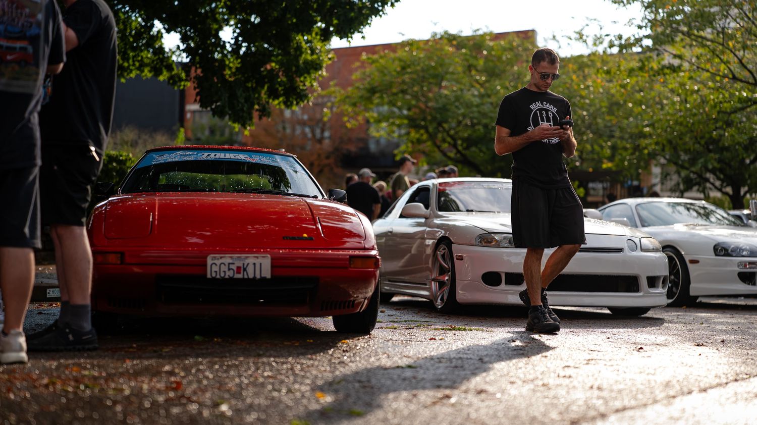 Panoramic view of car show with vehicles parked along urban street.