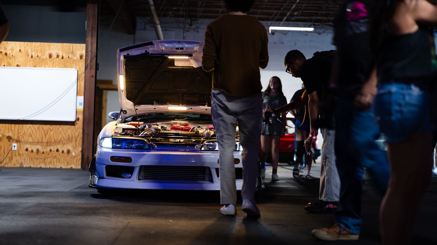 Car show in an indoor parking garage with colorful purple lighting and custom vehicles on display.