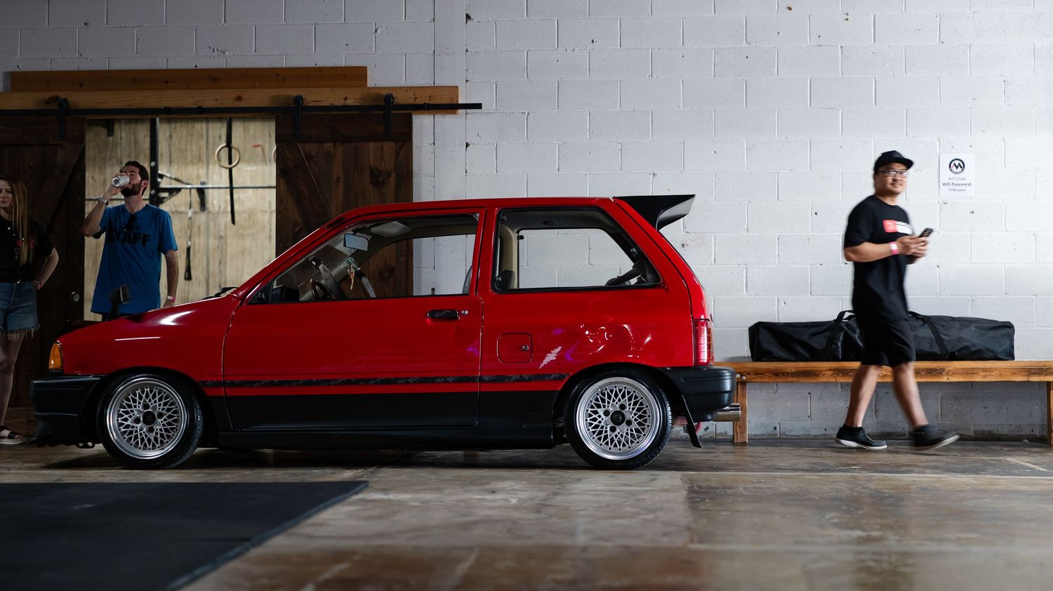 Modified red cars displayed against white industrial walls in a warehouse setting.