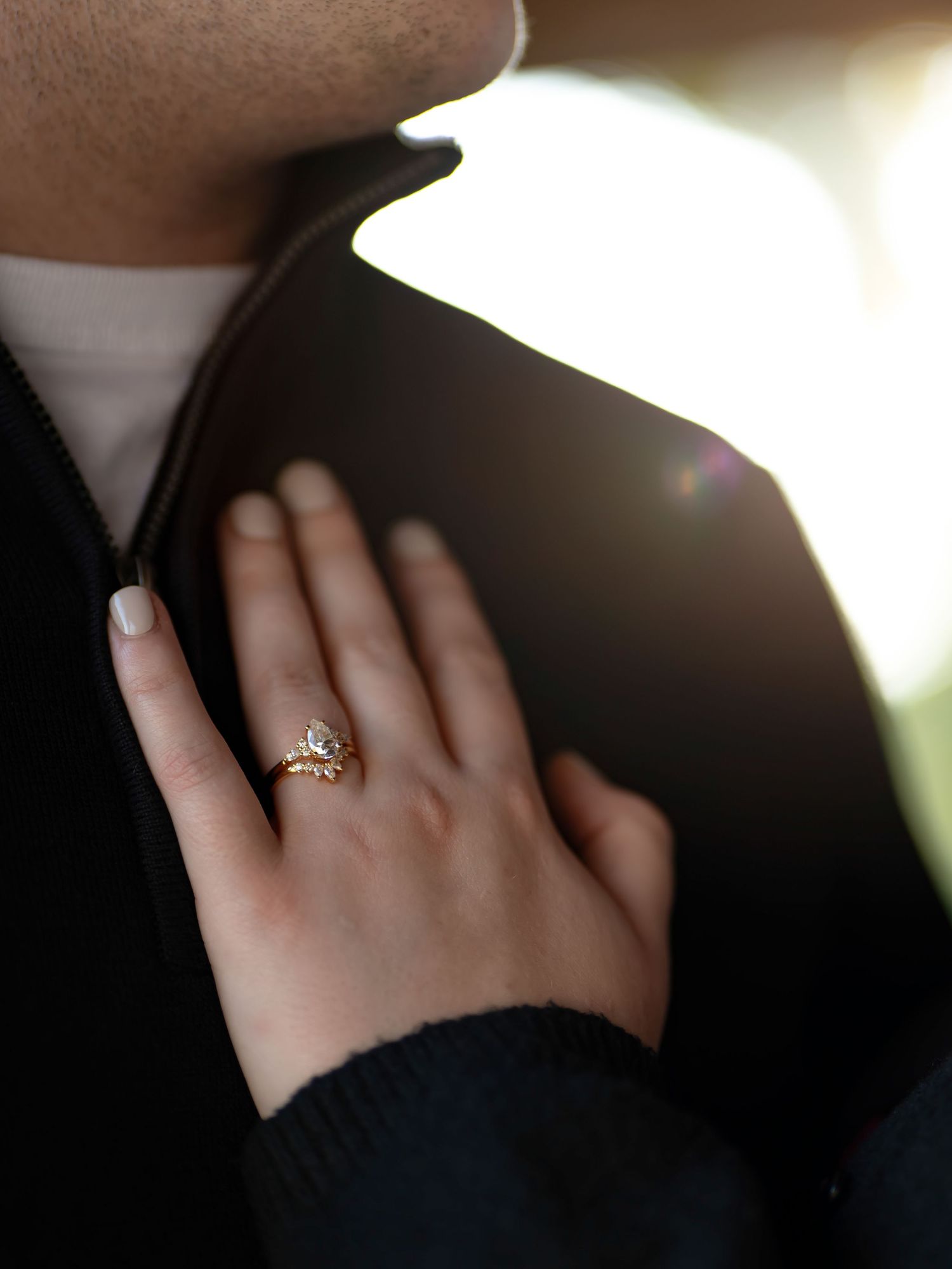 Close-up of an engagement ring on a hand against a dark background.