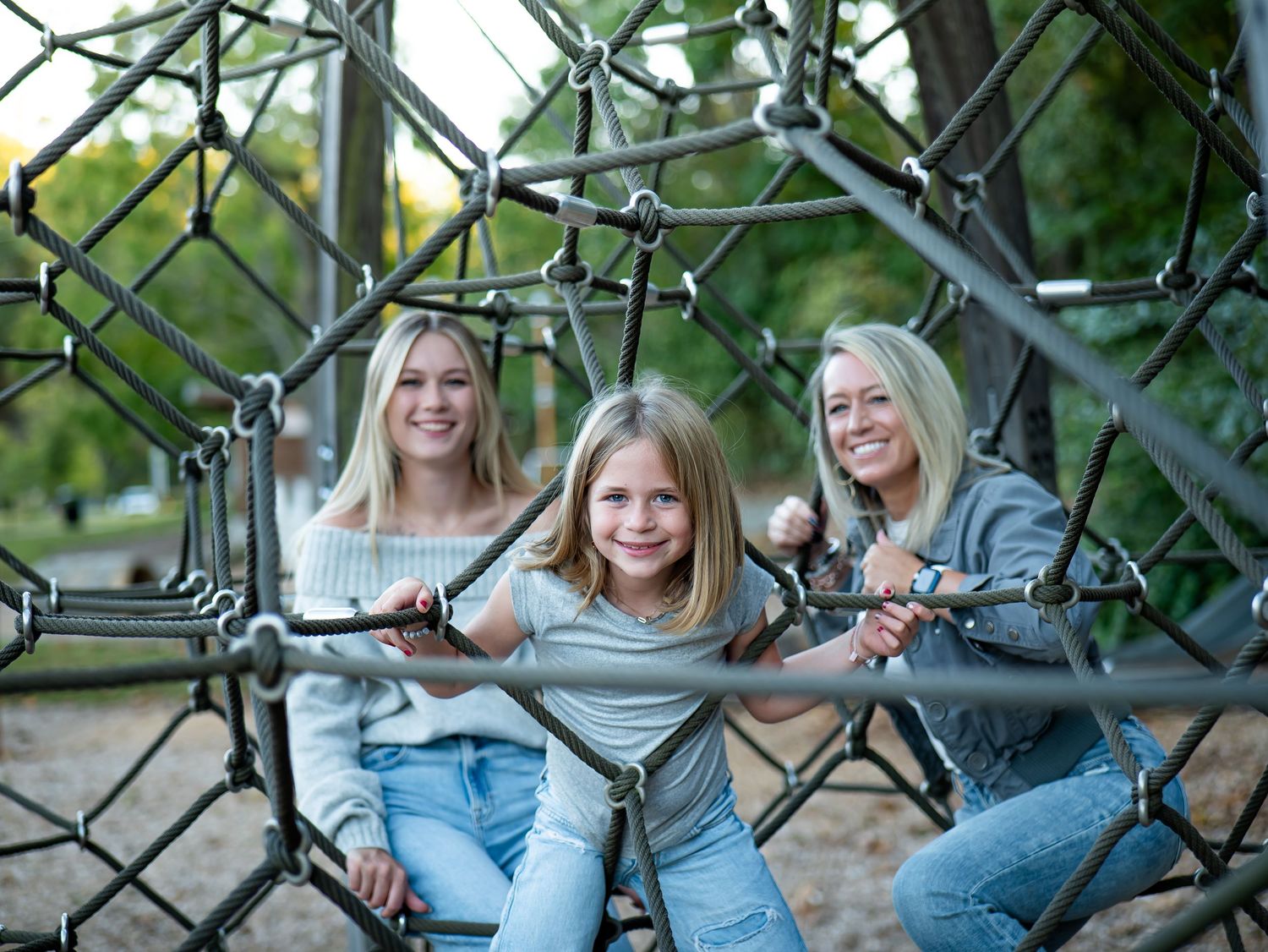People sitting and laughing together on a metal playground structure in a park setting.
