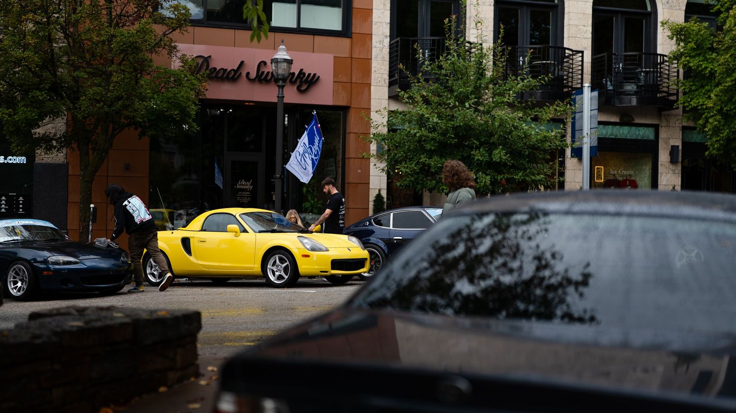 Cars displayed at an automotive gathering with brick buildings in the background.