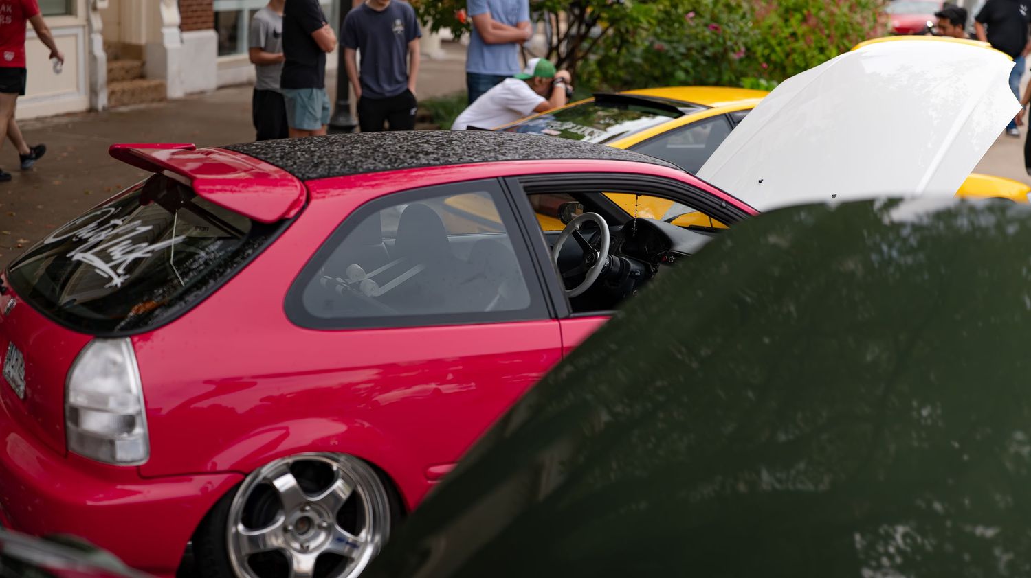 Modified sports cars in red and other colors displayed at an outdoor car show.