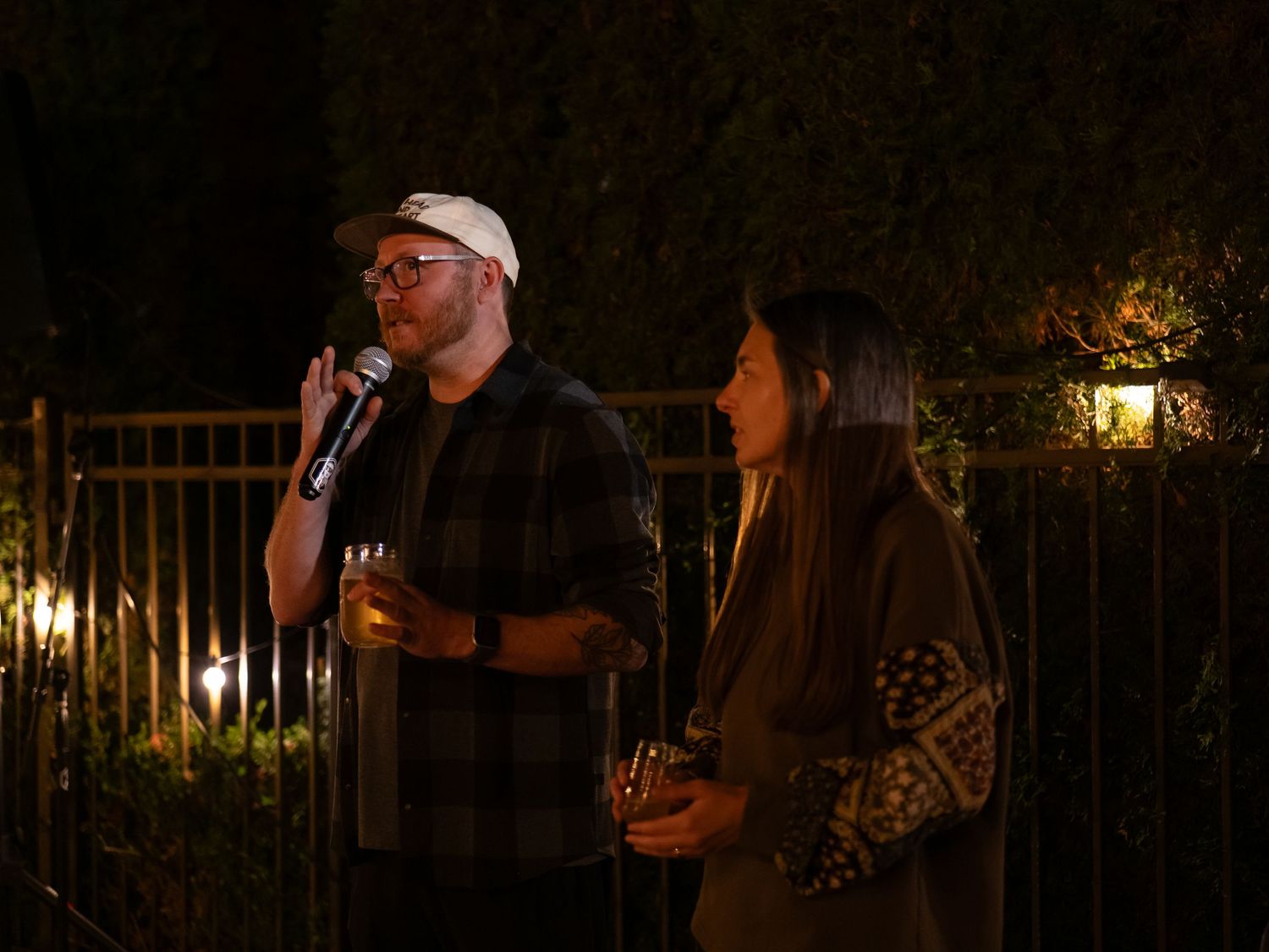 Musicians perform at a nighttime outdoor event with string instruments and microphones illuminated by warm lighting.