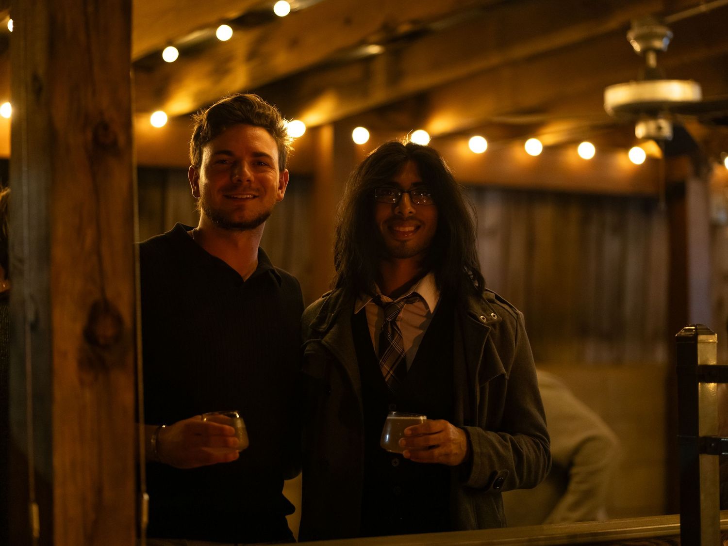 Group of people enjoying drinks at a dimly lit bar with string lights creating a warm, cozy atmosphere.