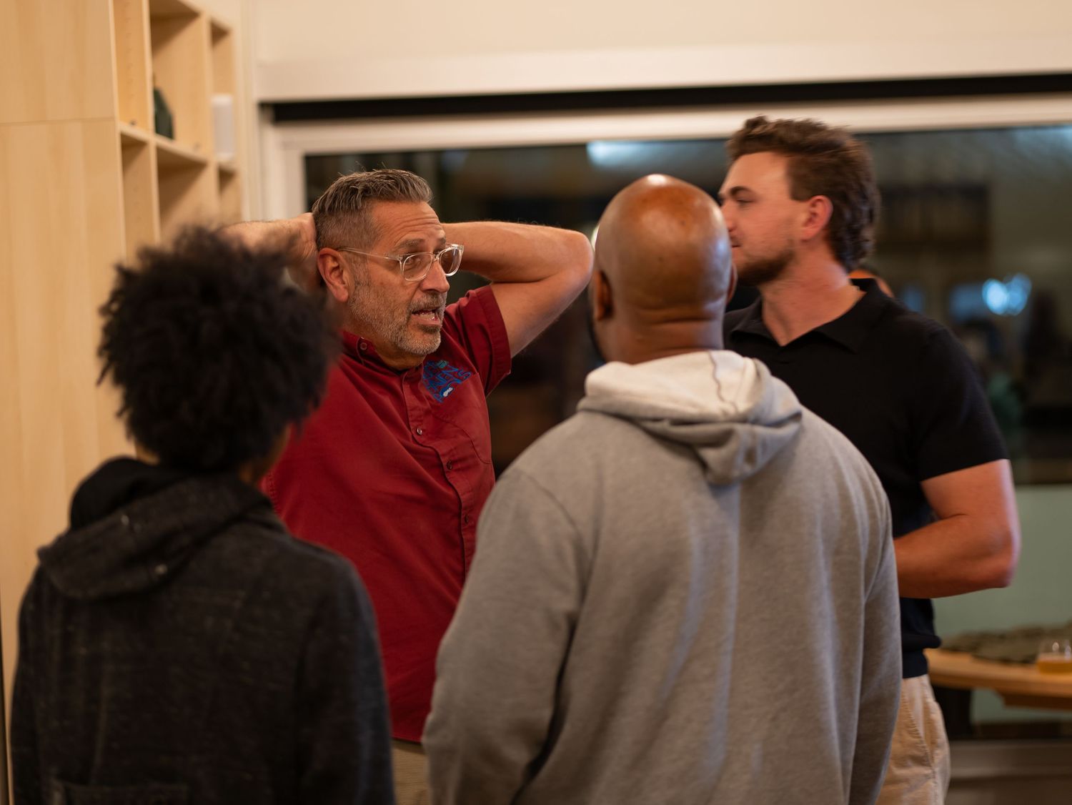 A group of people engaged in casual conversation in what appears to be a dimly lit indoor space.