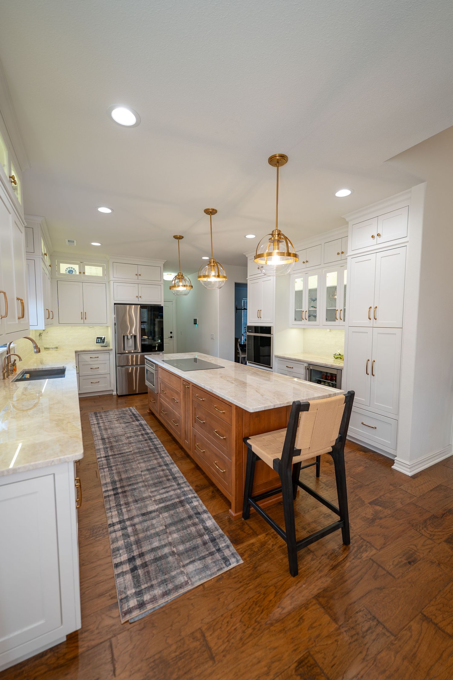 Modern kitchen with white cabinets, wood island, marble countertops, gold pendant lights, and hardwood floors.