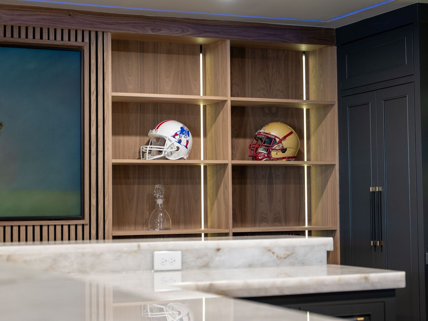 Modern built-in wooden shelving unit displaying football helmets above a marble kitchen island.