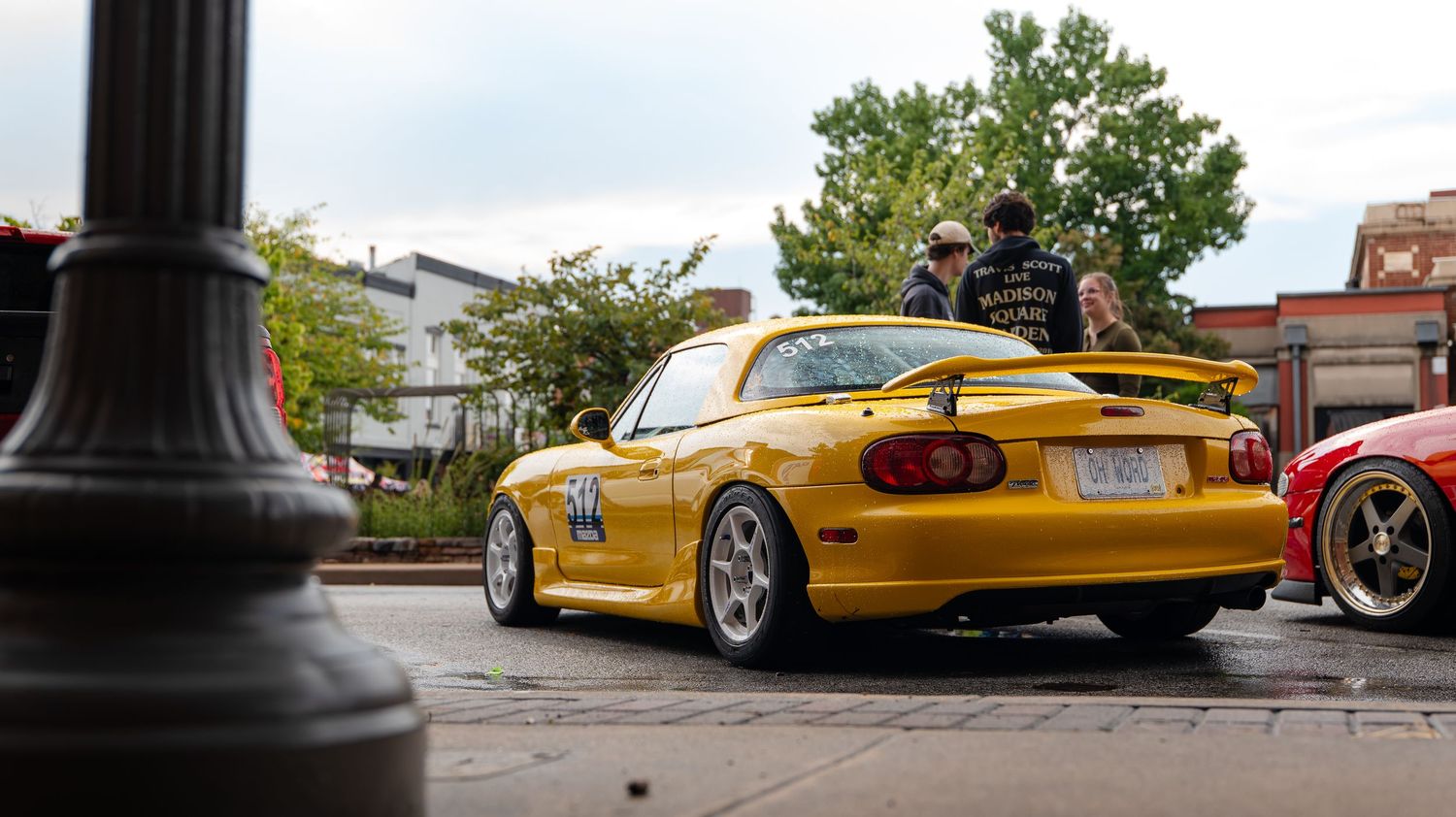Yellow Mazda Miata with aftermarket modifications parked on city street.