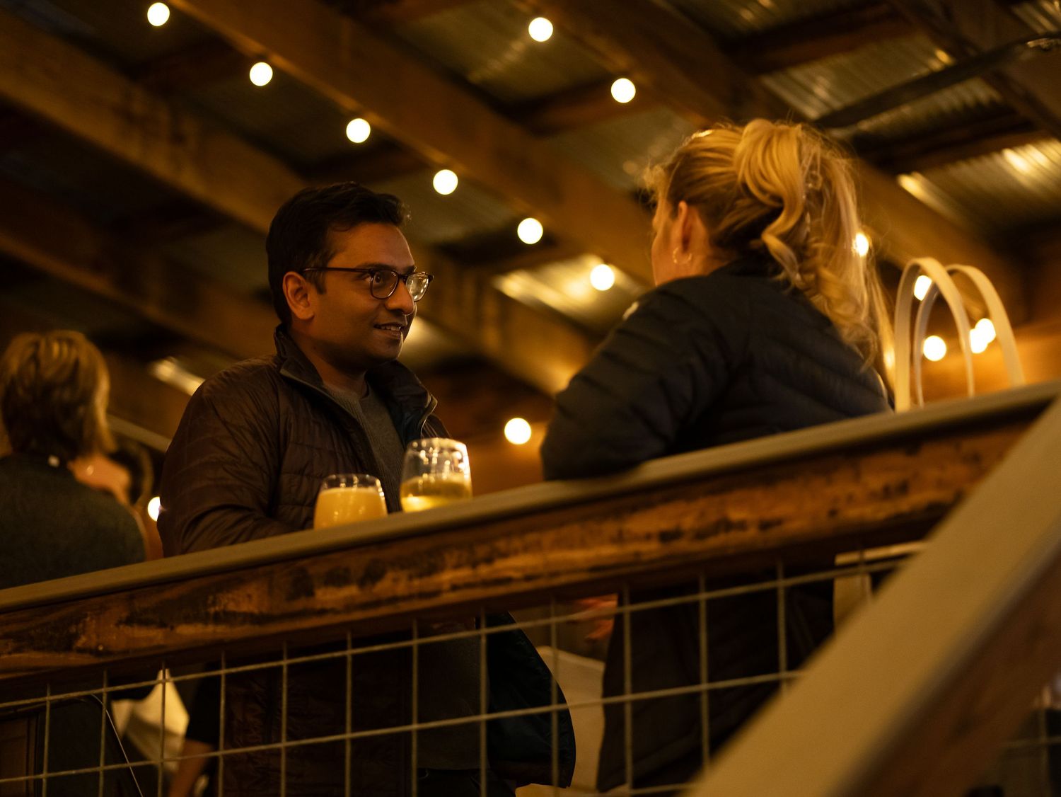 People enjoy drinks at a dimly lit bar with overhead string lights creating a warm, intimate atmosphere.