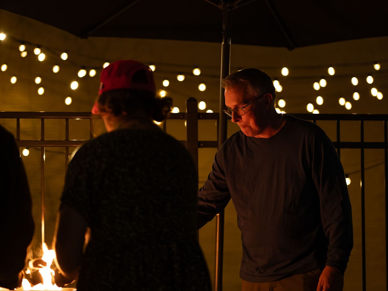 Two people stand on a patio at night under string lights and an umbrella creating a cozy outdoor atmosphere.