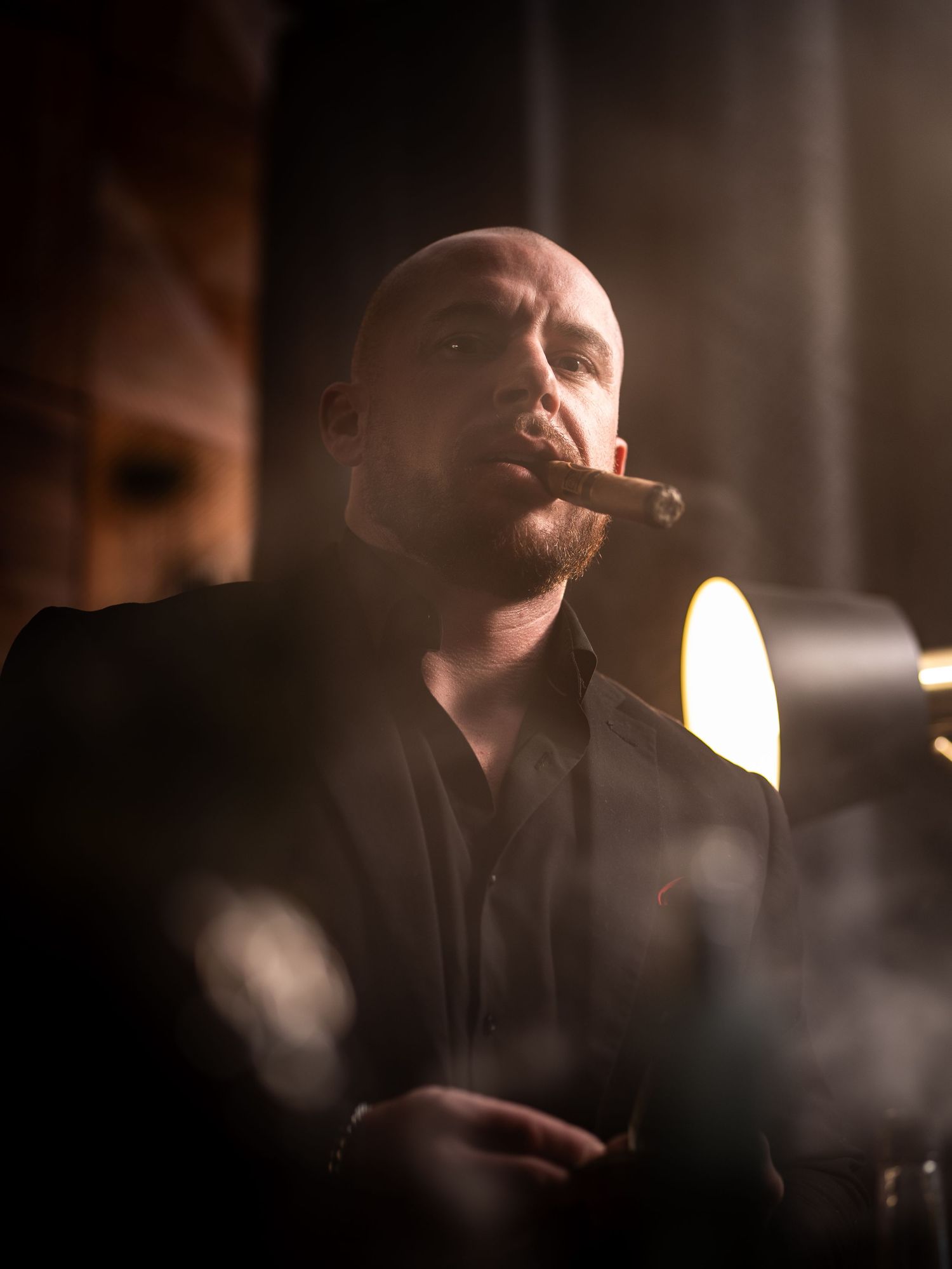 Moody portrait of a person smoking a cigar in dark lighting with dramatic shadows and warm ambient glow.