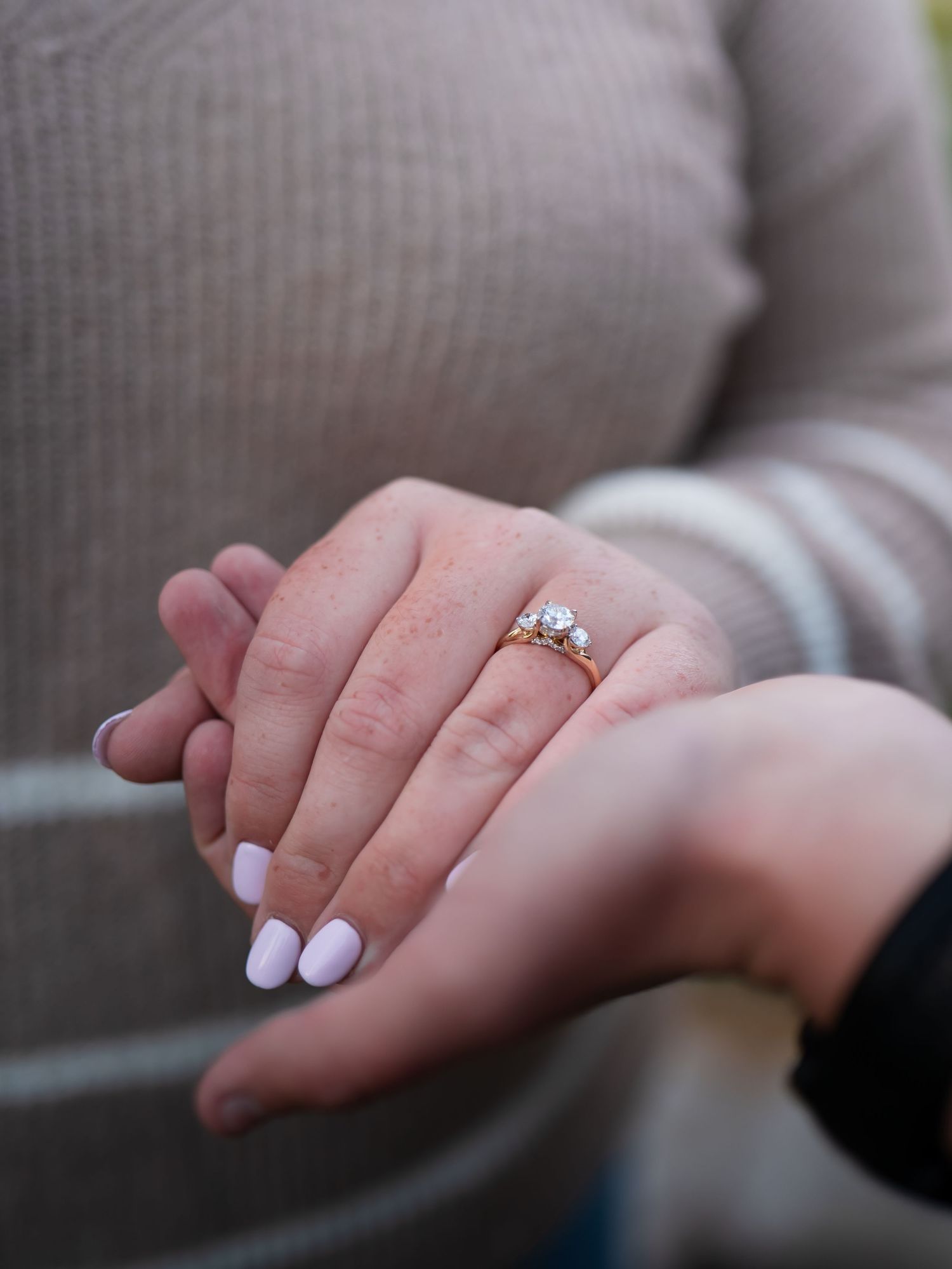 A close-up series of hands with white nail polish showing a diamond engagement ring on a gray background.
