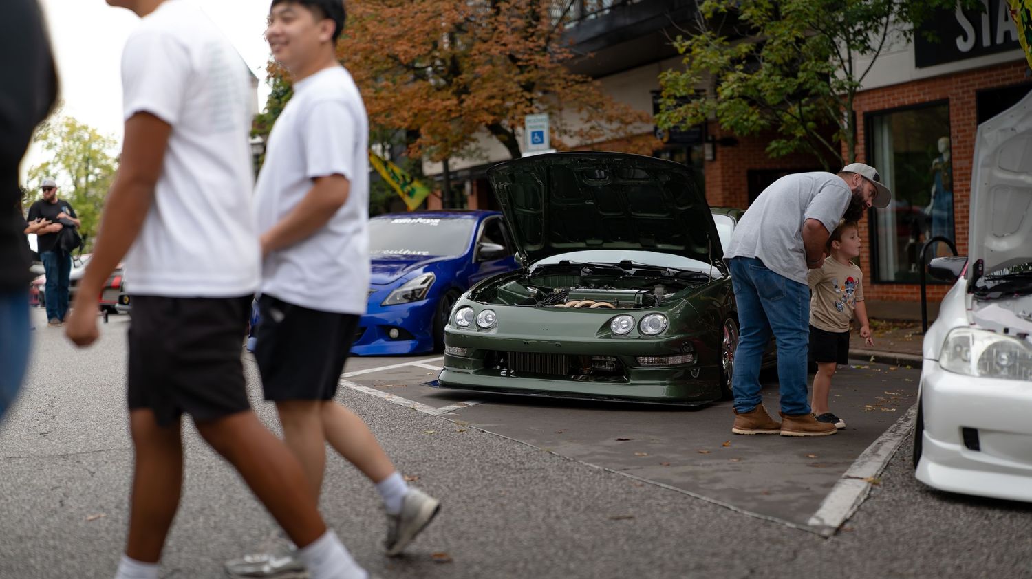 Row of modified cars displayed at a daytime car show with spectators walking by.