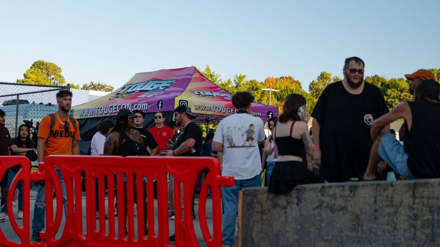 Car enthusiasts gathered at an outdoor event with red barriers.