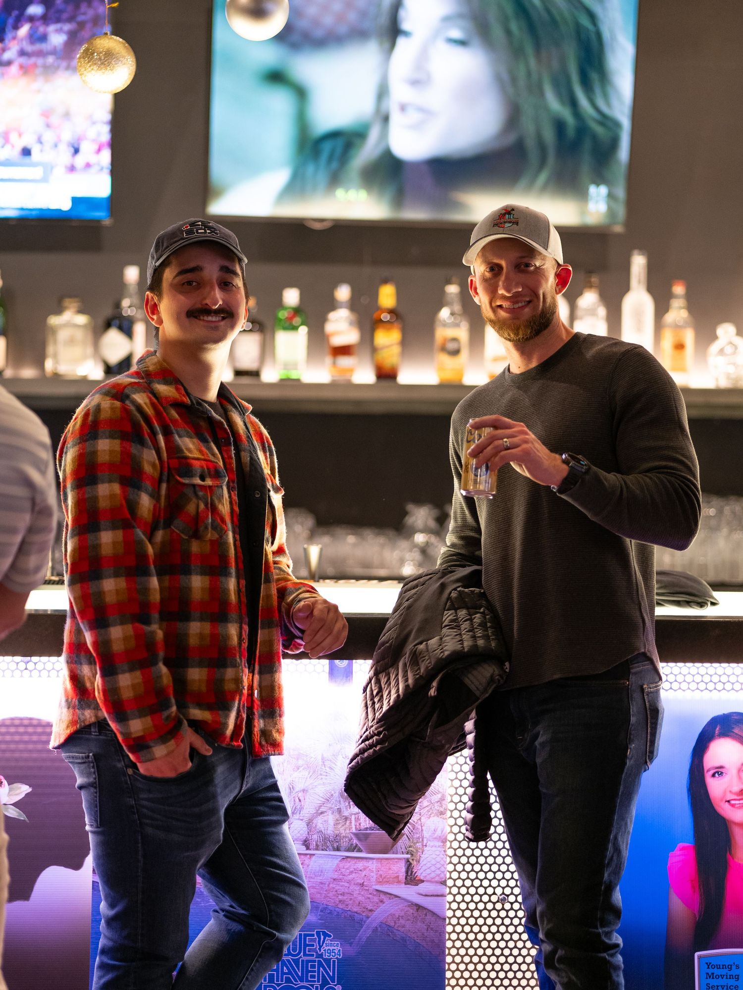 People socializing at a bar with illuminated bottles and neon lighting in the background.