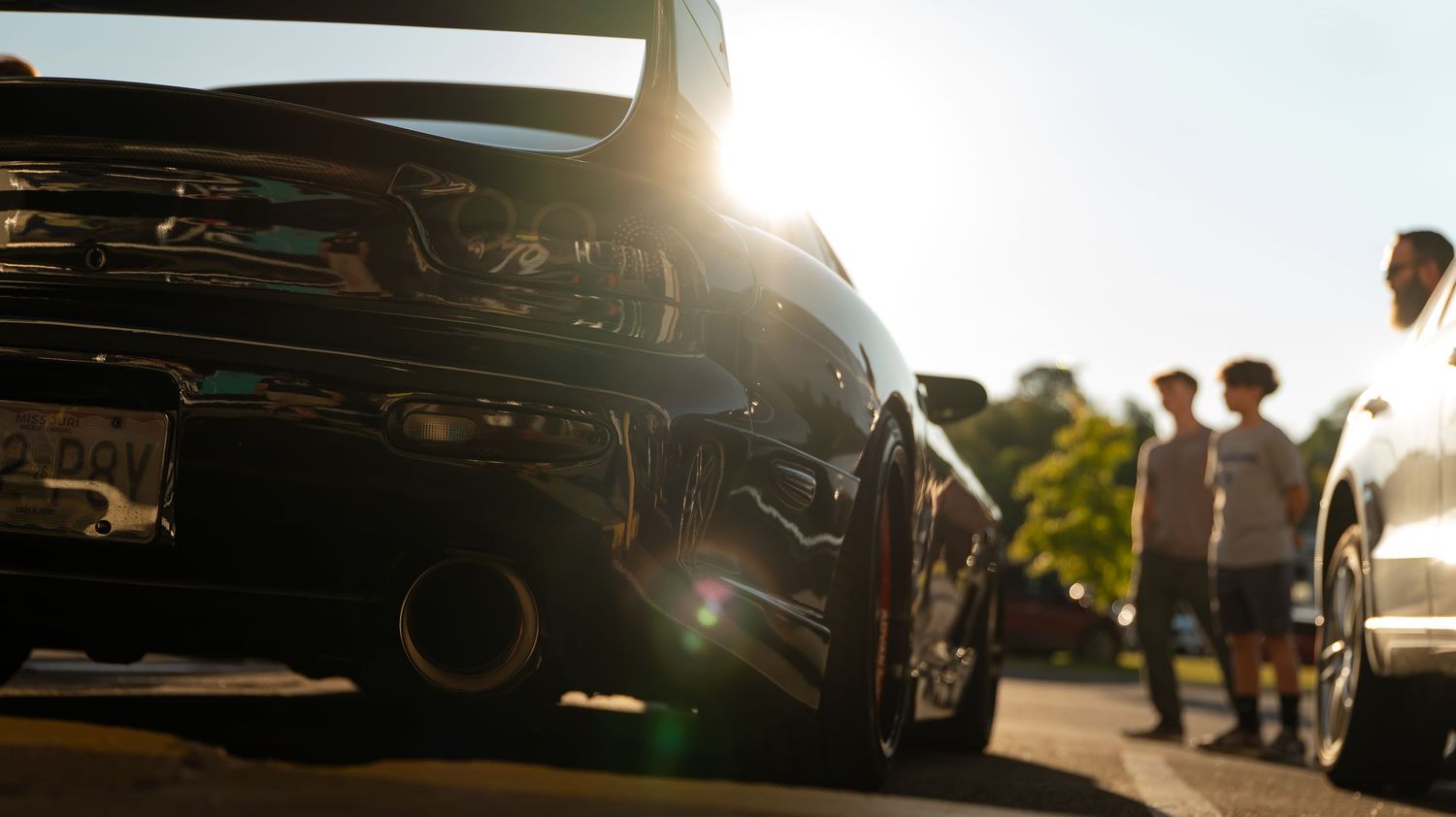 Silhouetted view of cars and people at a sunset car meet.