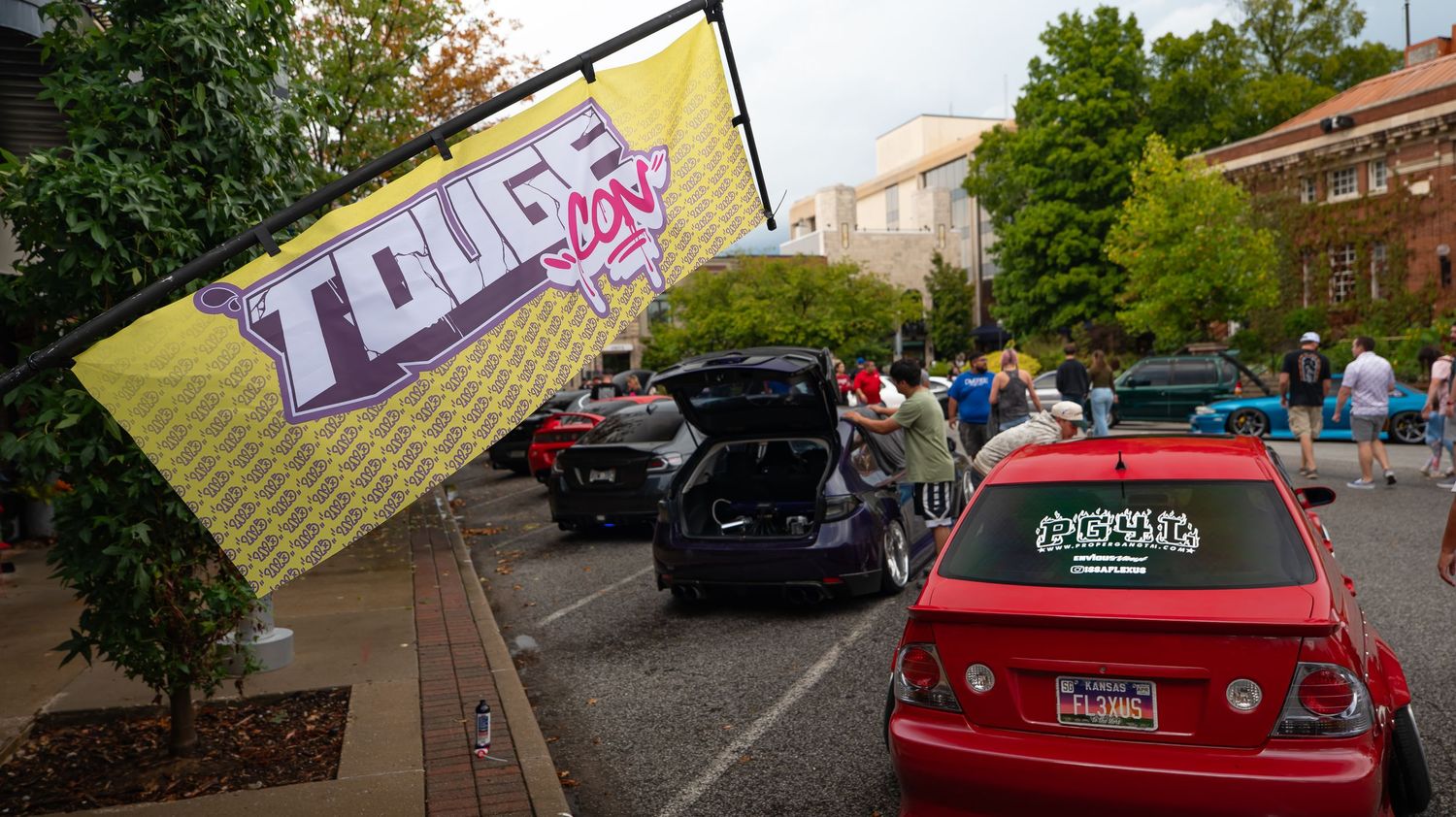 Panoramic view of a red sports car parked on a street with trees and buildings in the background.