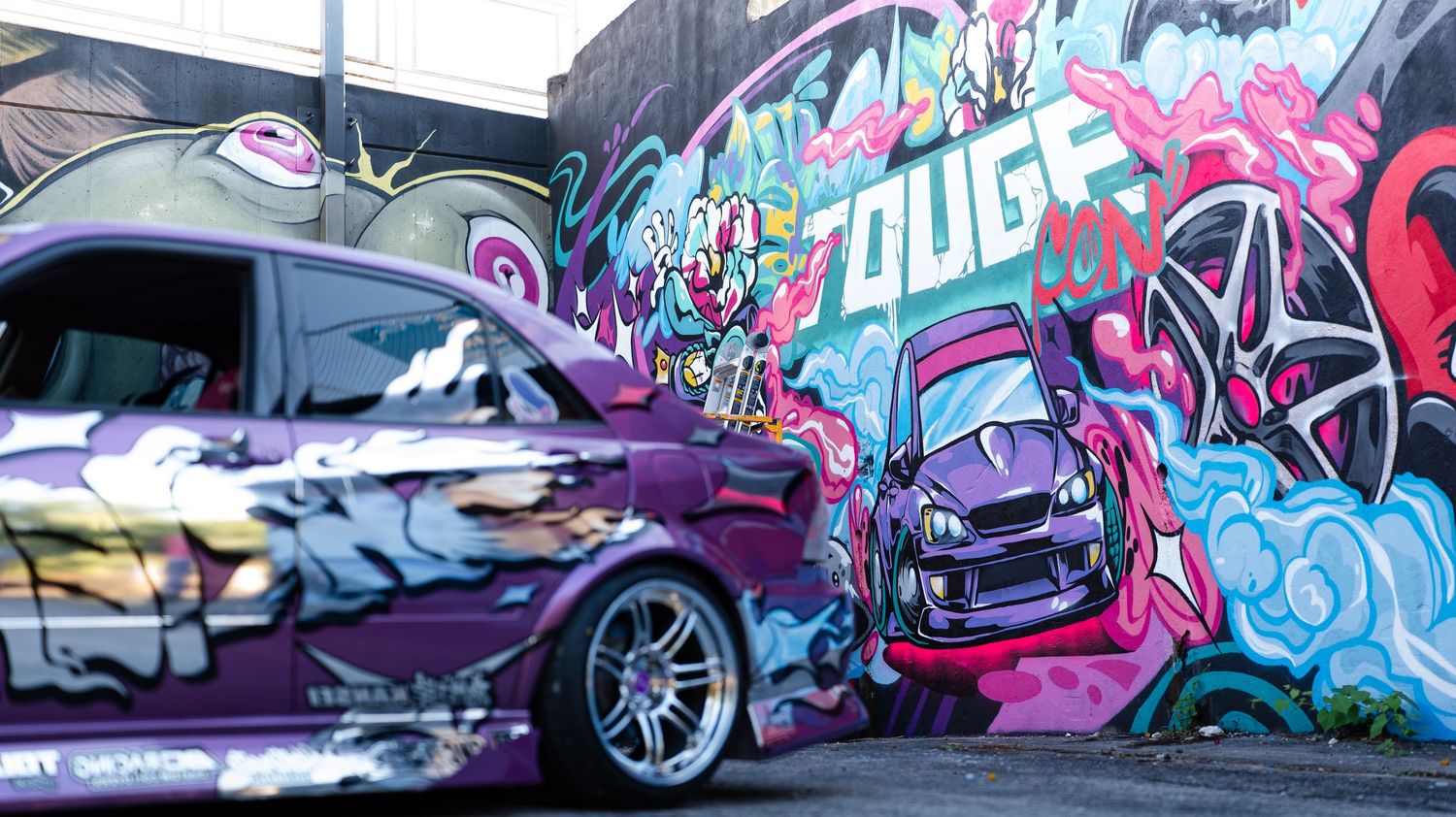 Colorful graffiti mural stretching across a long wall with cars parked alongside.