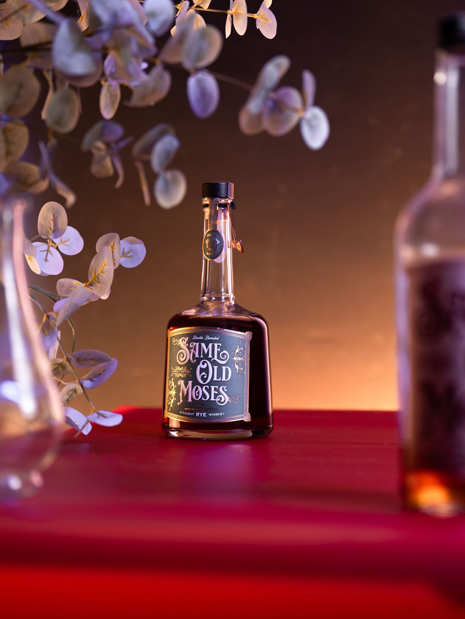 A Jim Beam bourbon whiskey bottle sits elegantly against a dark background with soft purple bokeh lights and red surface.