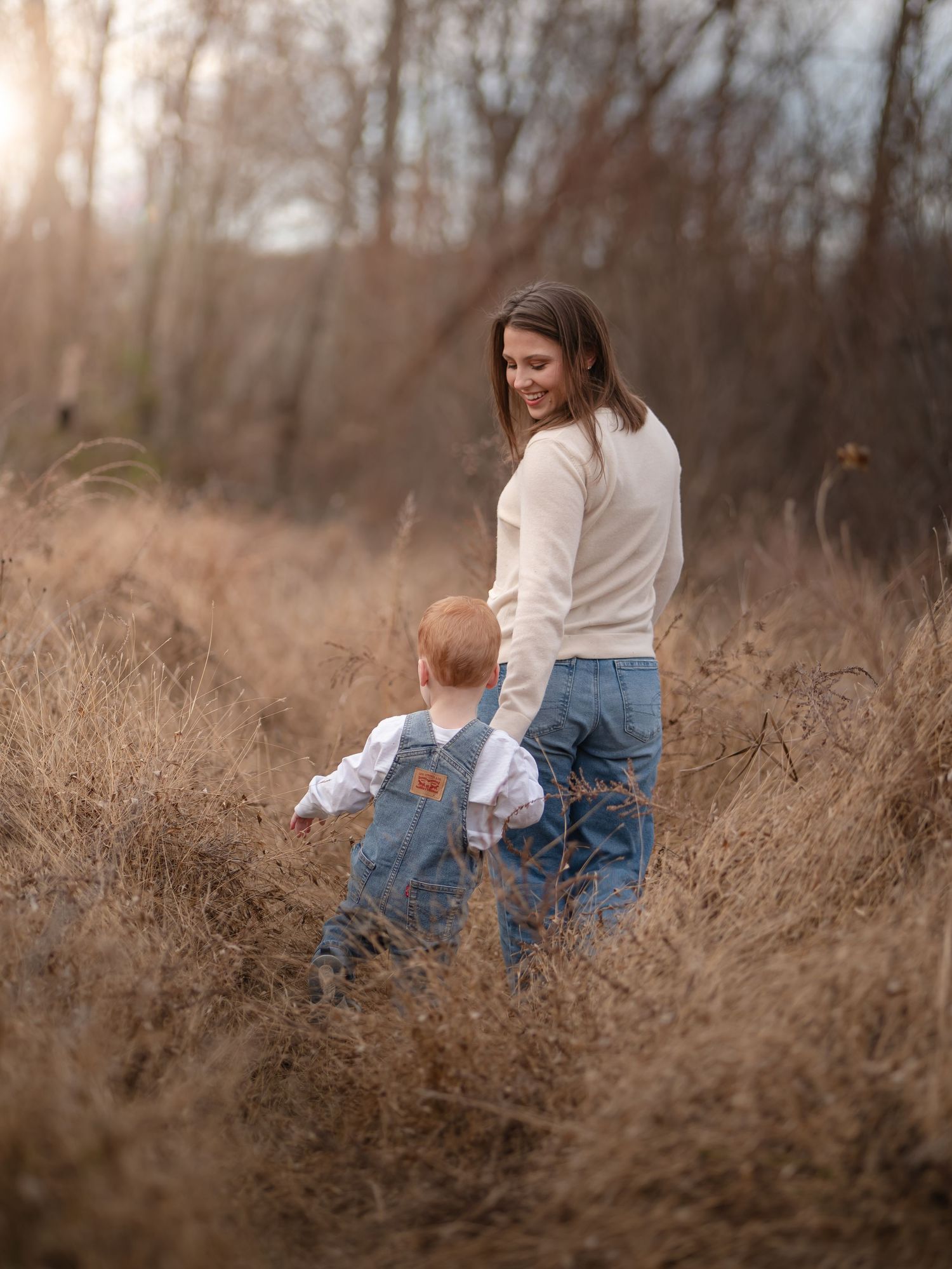 A person in a cream sweater and jeans sits thoughtfully in tall autumn grass during golden hour.