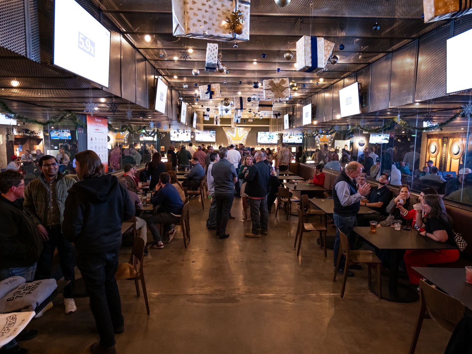 A busy food hall interior with wooden tables and industrial decor filled with dining customers.
