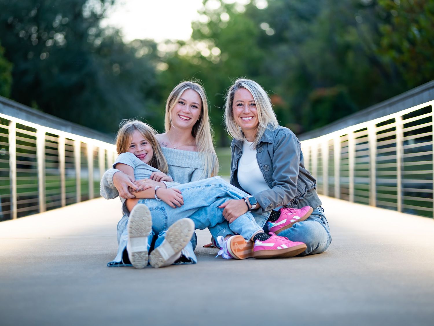 Family in casual clothing lying on wooden bridge during sunset photo session in park.