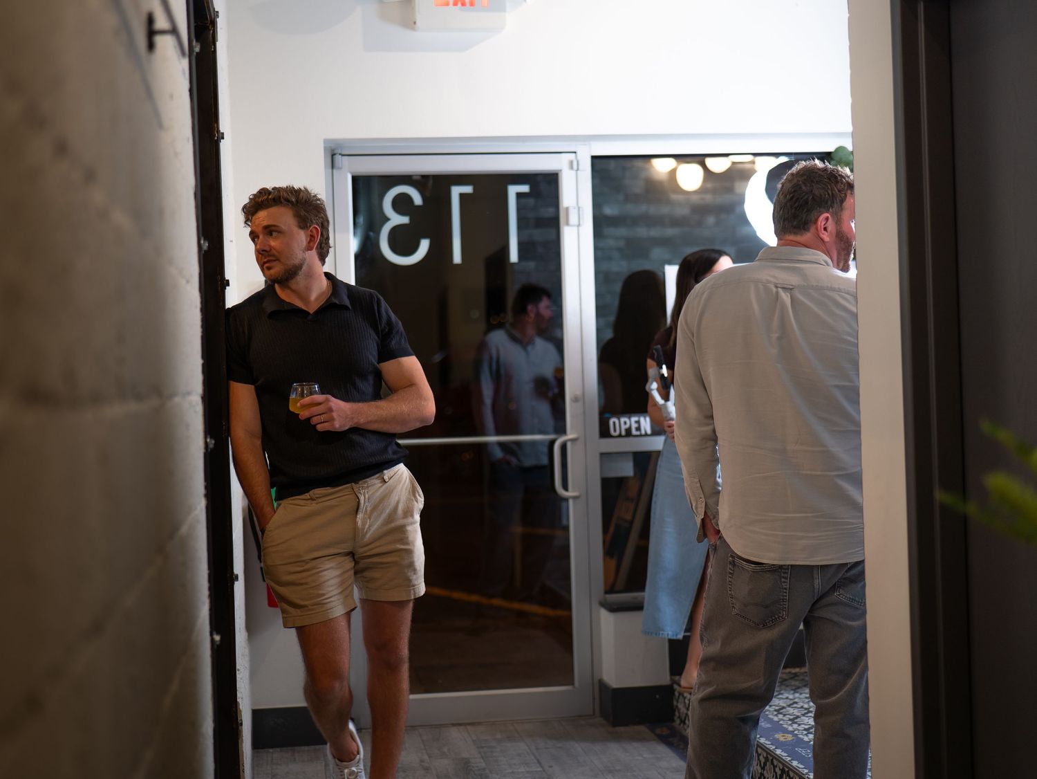 People gathered in a hallway or lobby area near glass doors and walls.