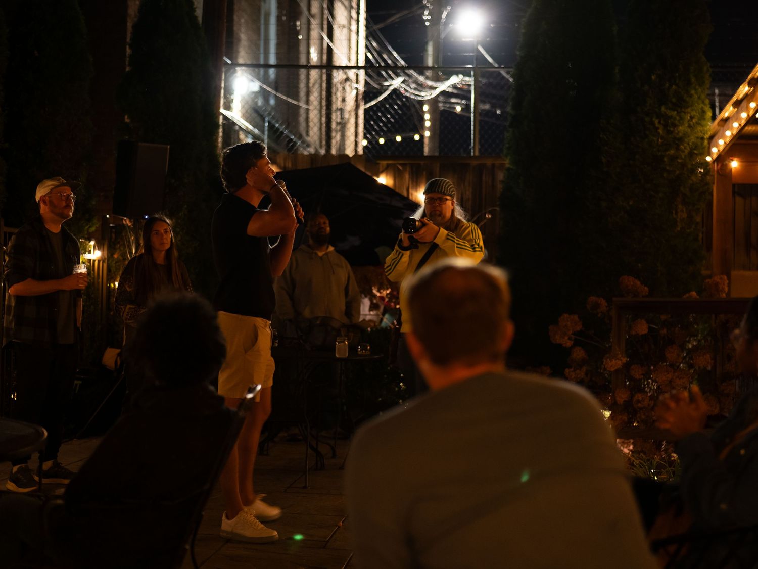 Musicians perform on a dark street corner at night with string instruments while a crowd gathers to listen.