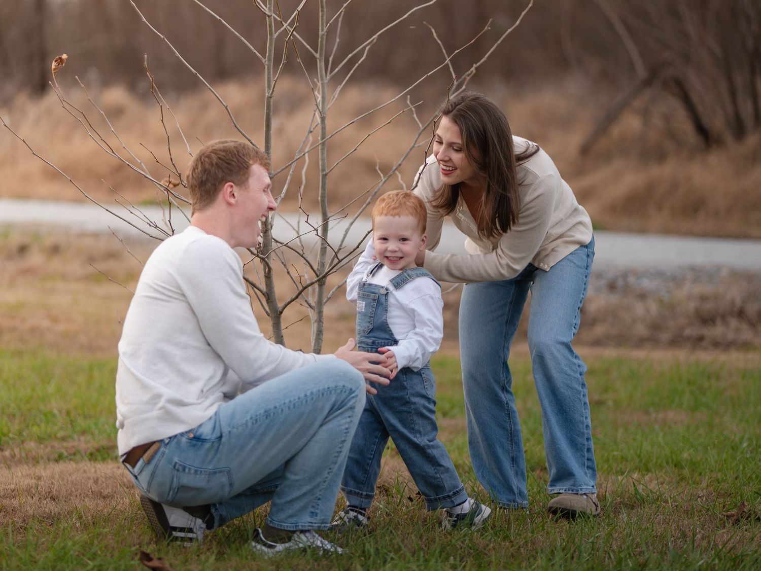 A family sits together outdoors on grassy ground during a casual photo session in natural lighting.
