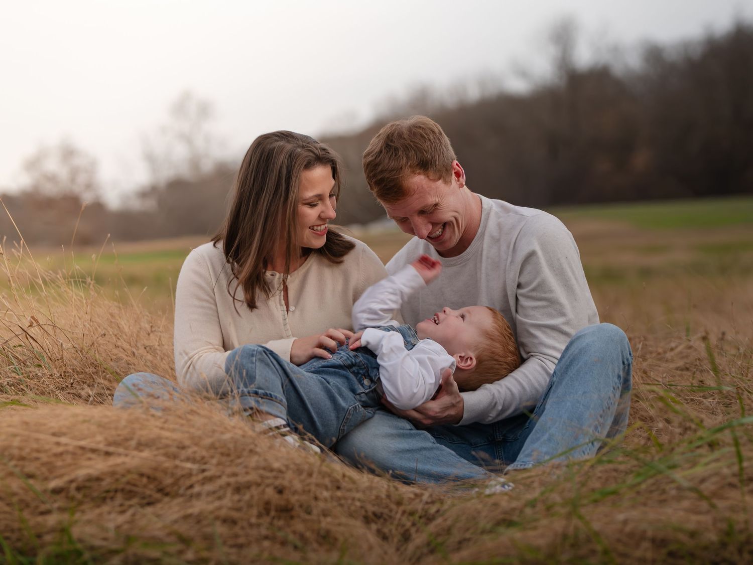 A couple and their baby share tender moments while laying in a golden autumn field during sunset.