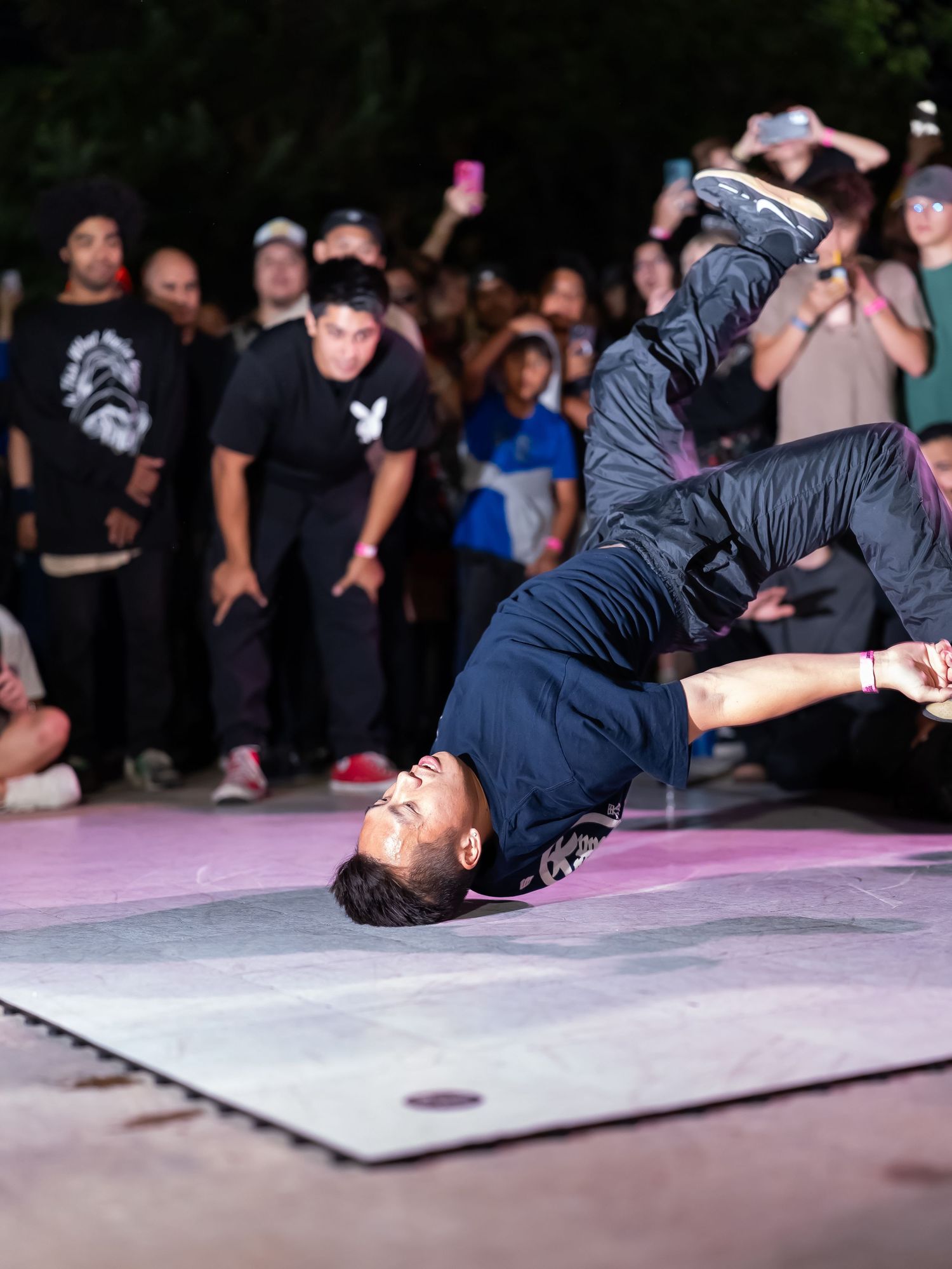 Breakdancer performing acrobatic moves on stage with crowd watching in background.
