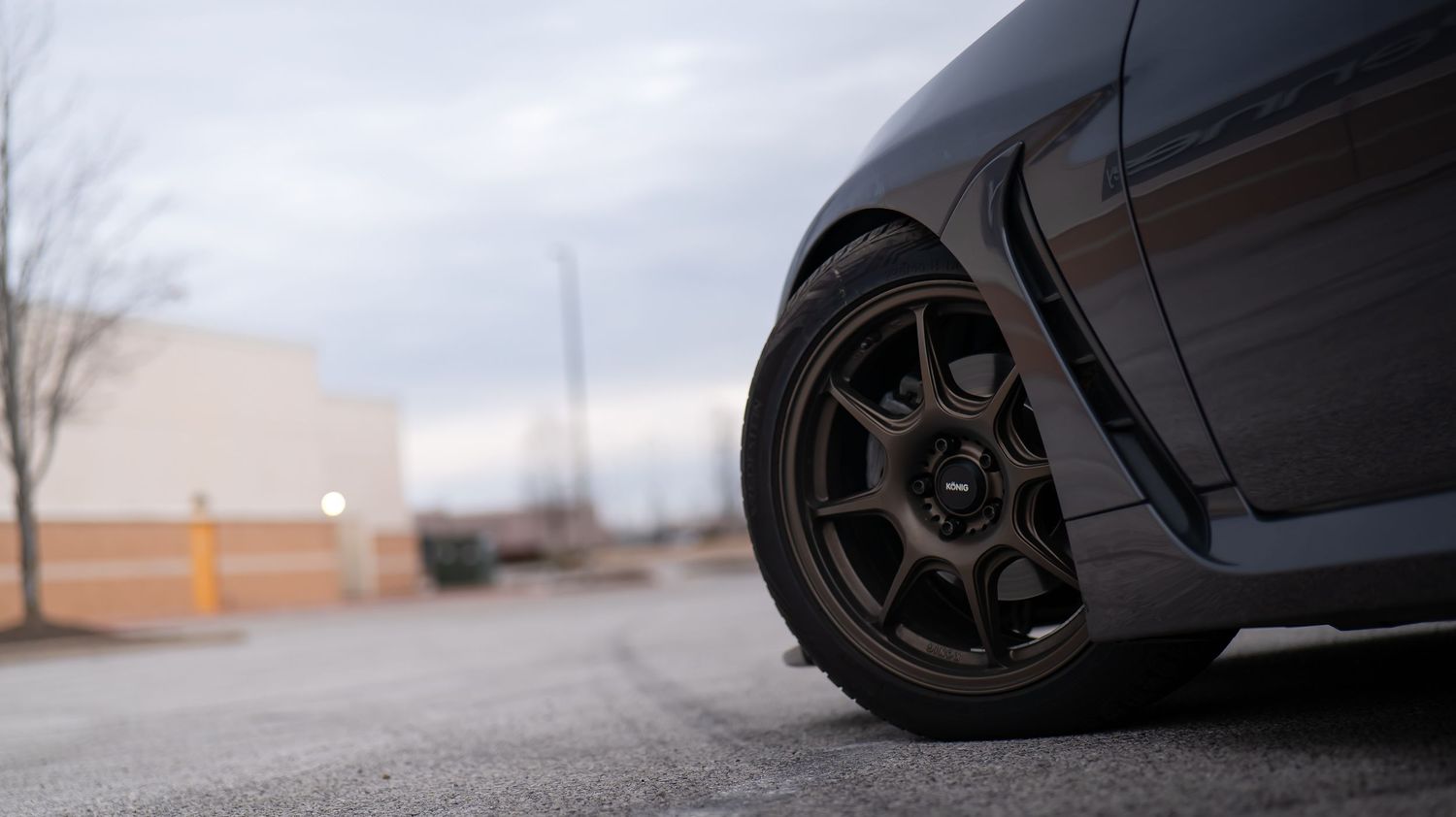 Low angle shot of a modified sports car's wheel and suspension setup on asphalt.