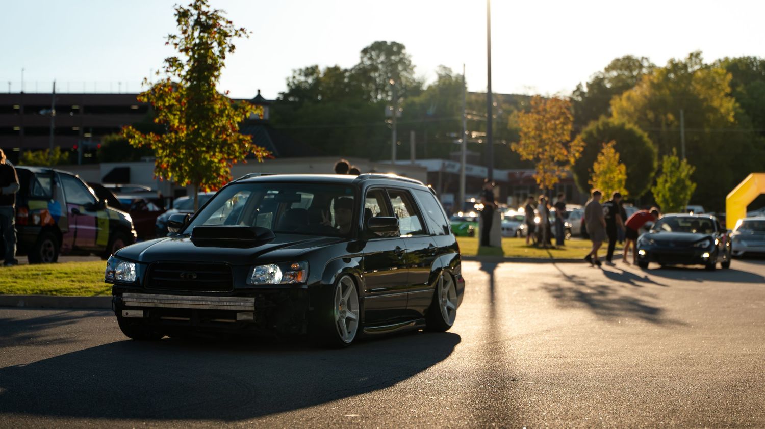 Panoramic shot of a parking lot filled with performance cars during golden hour.