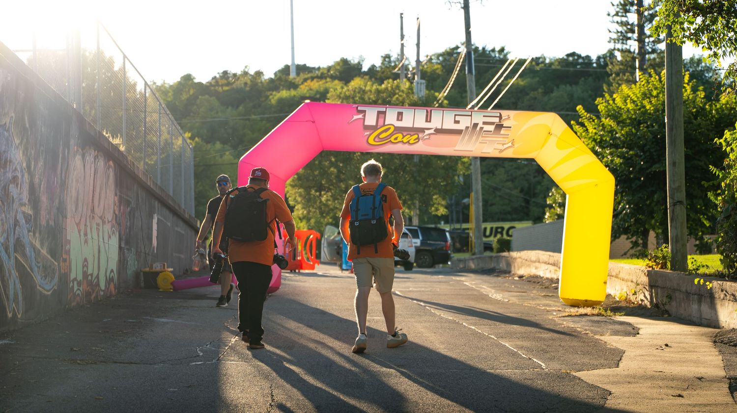 Wide panoramic shot of a car meet with pink and yellow event banners.