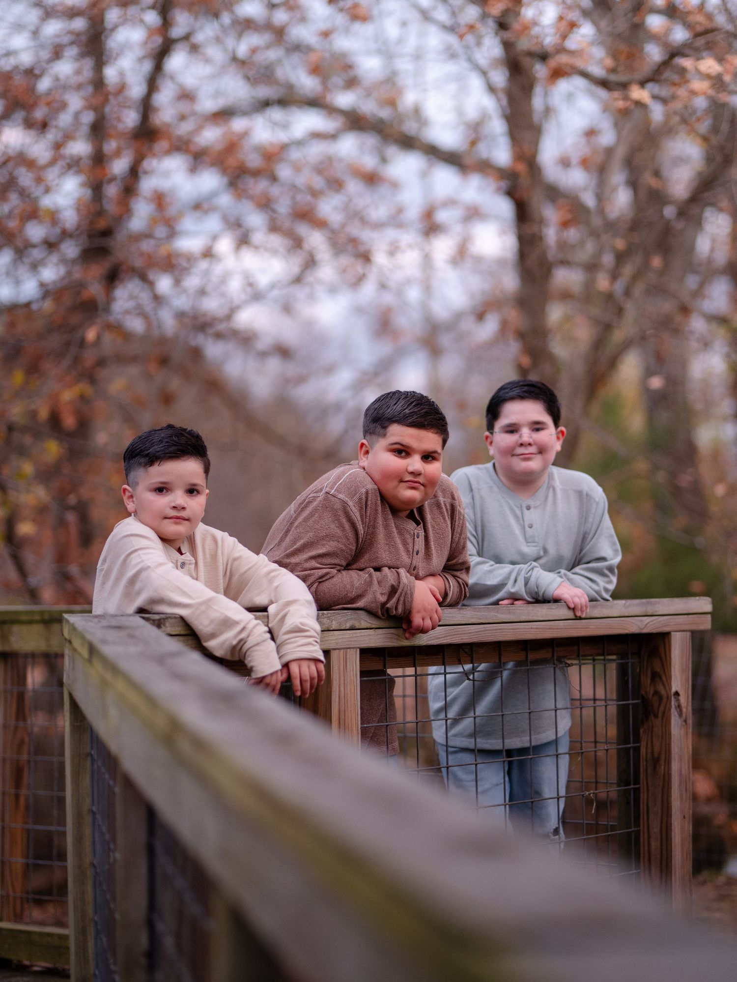 Young people leaning on a wooden railing outdoors during autumn with fall foliage in the background.