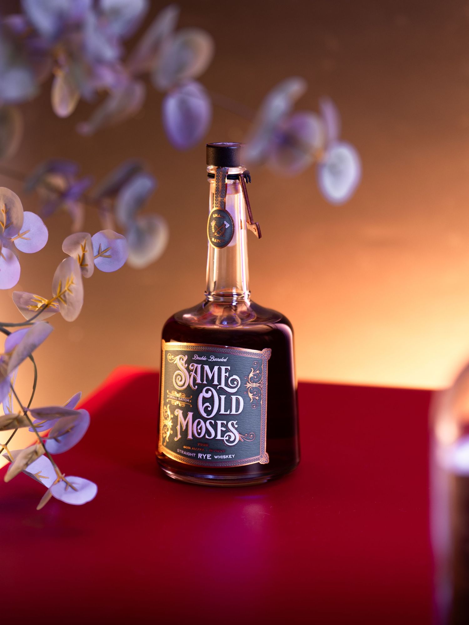 A series of whiskey bottles photographed with artistic bokeh lighting effects against a red and brown background.