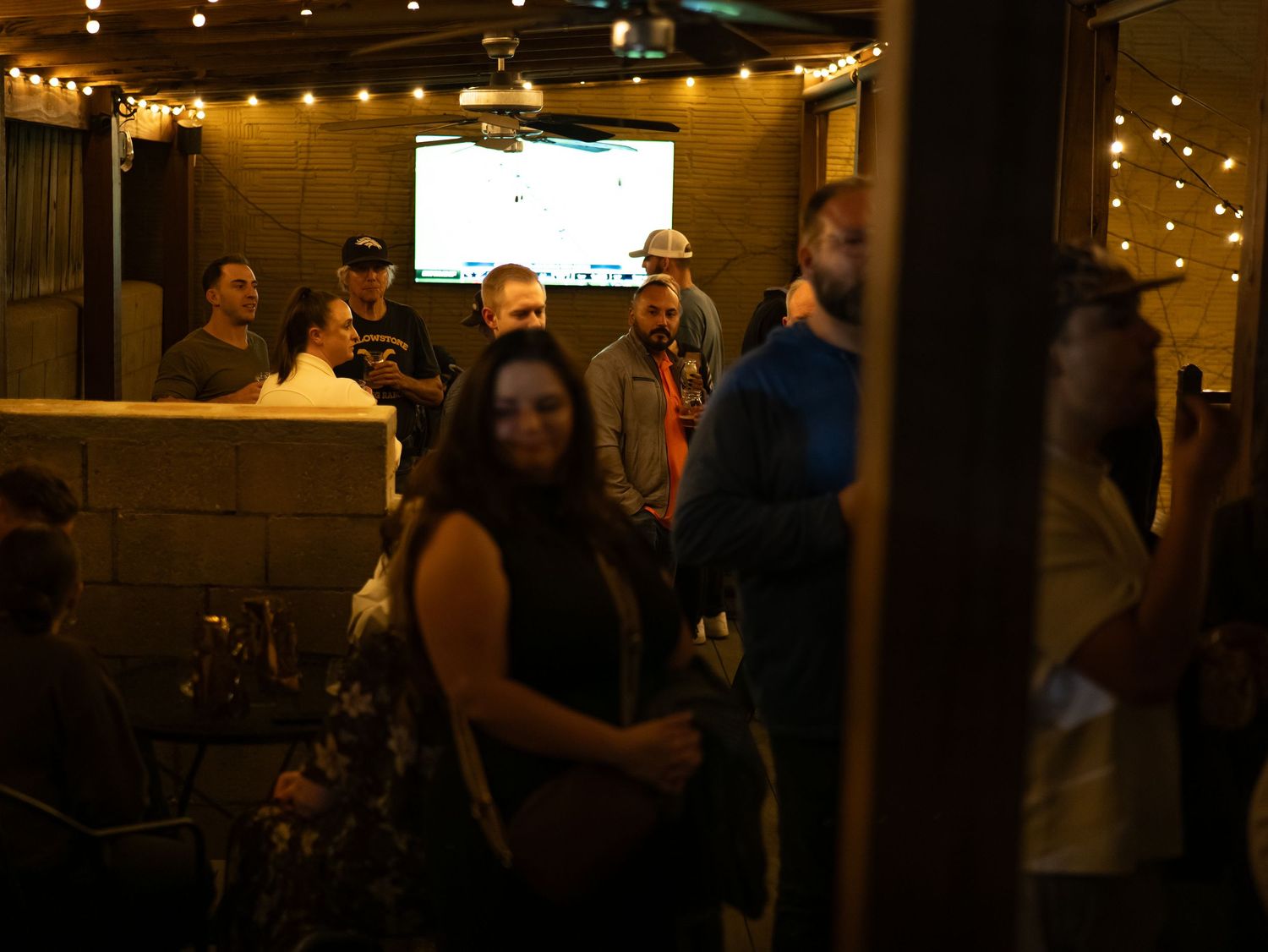 People enjoying drinks and conversation at a dimly lit bar with string lights creating a warm ambiance.