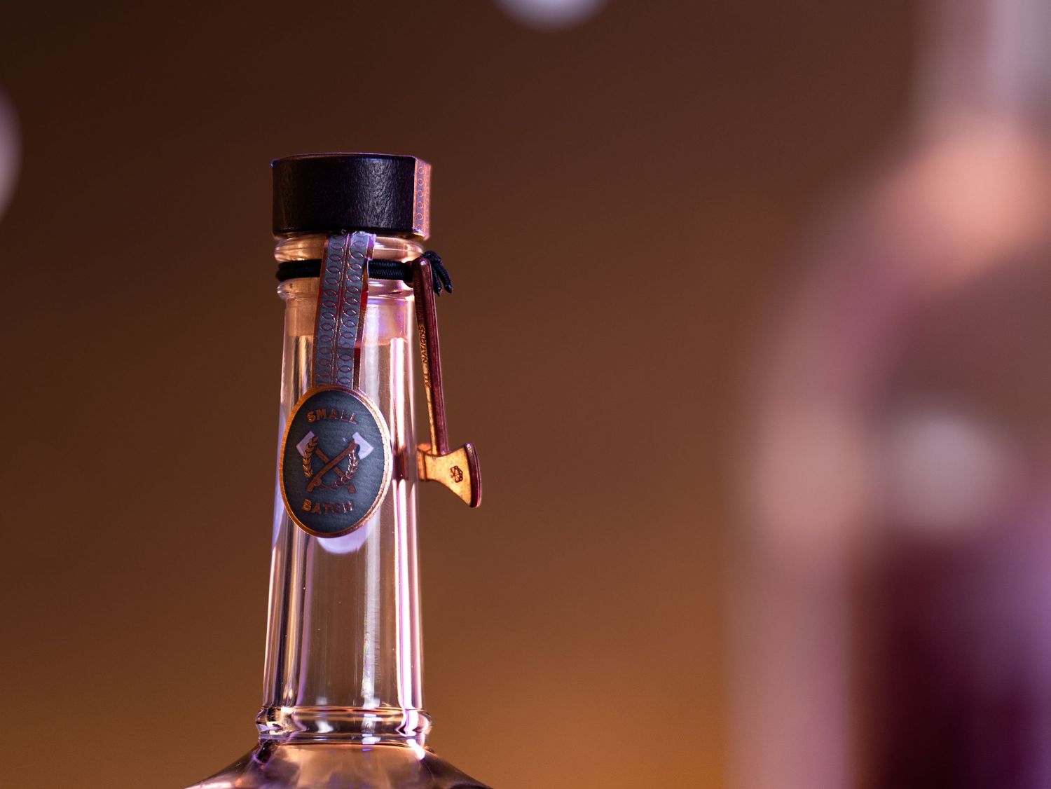 A glass of red wine sits in front of a blurred warm-toned background with bokeh lighting effects.