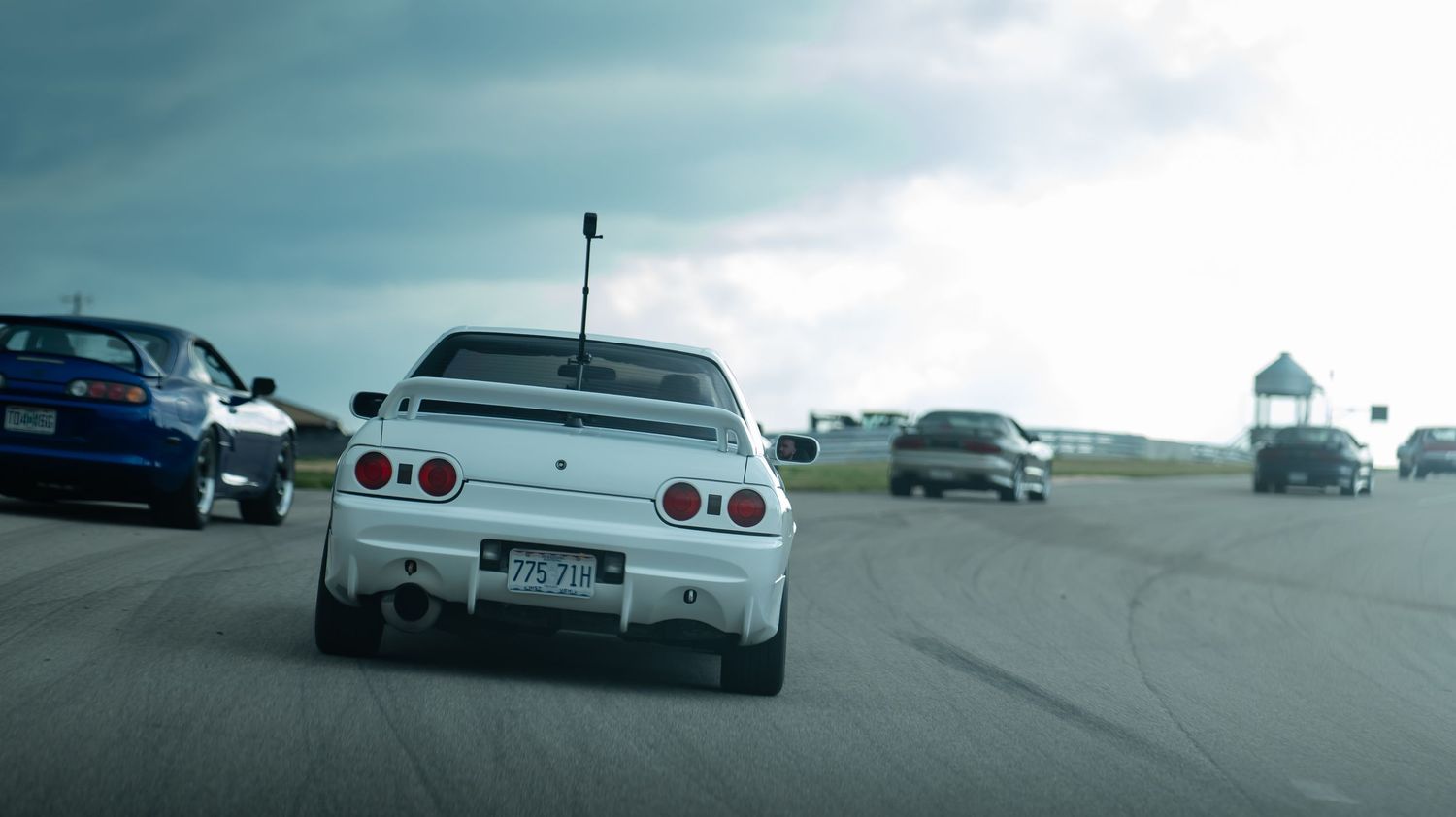 Multiple vintage Nissan Skyline GT-R cars lined up at a car show under cloudy skies.