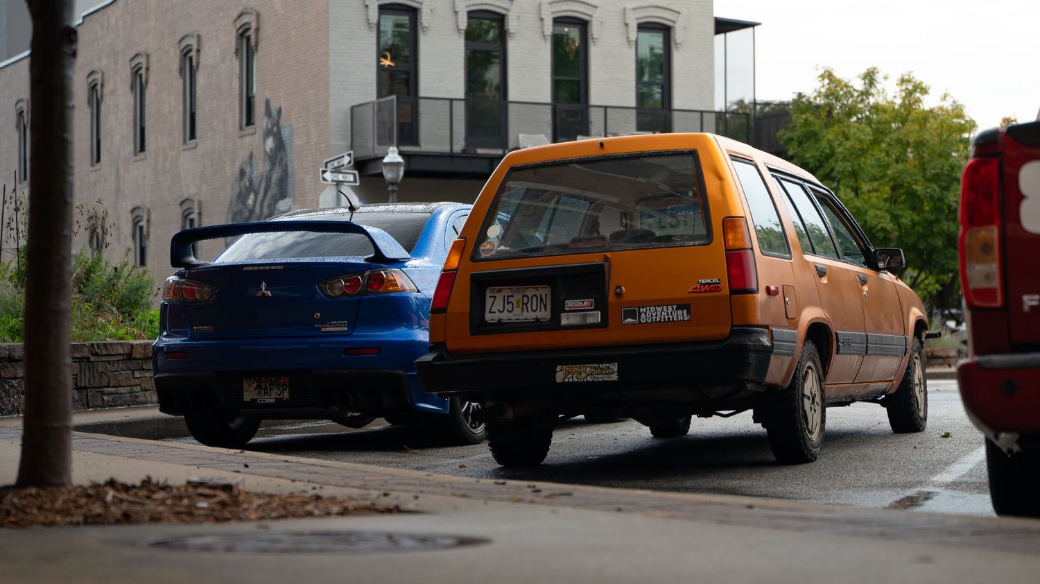 Street view of urban buildings with parked cars along the curb.