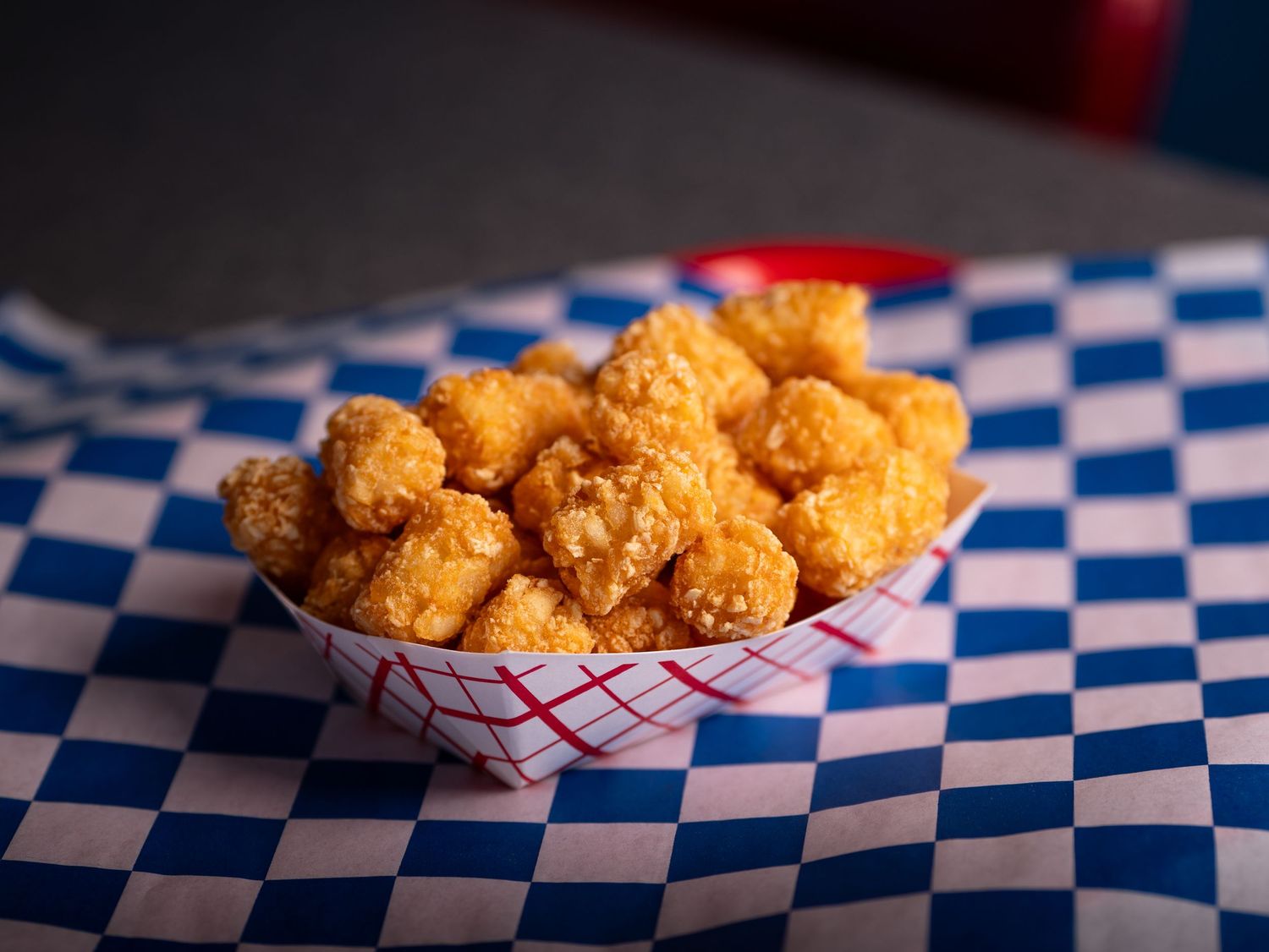 Golden crispy tater tots arranged in a paper-lined basket on a blue and white checkered surface.