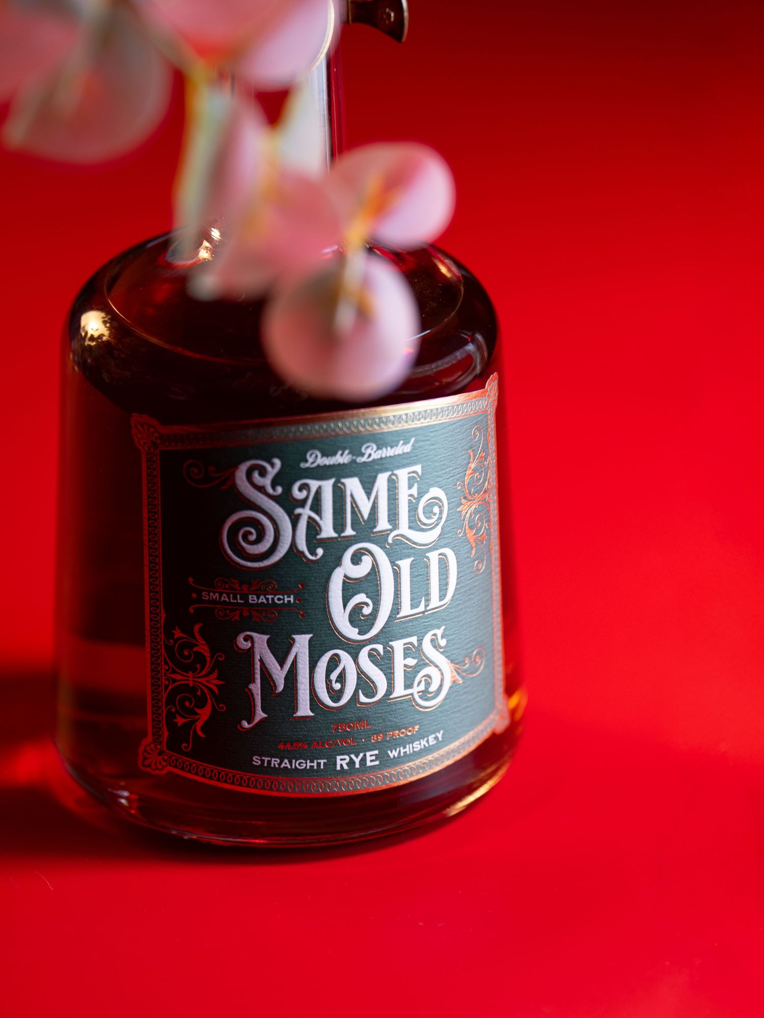 A bottle of Saint Moses Straight Rye Whiskey photographed against a vibrant red background with dramatic lighting.